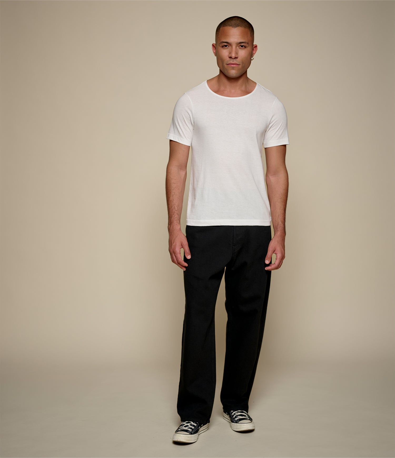Man wearing a white loopwheeled t-shirt and black pants on a beige background