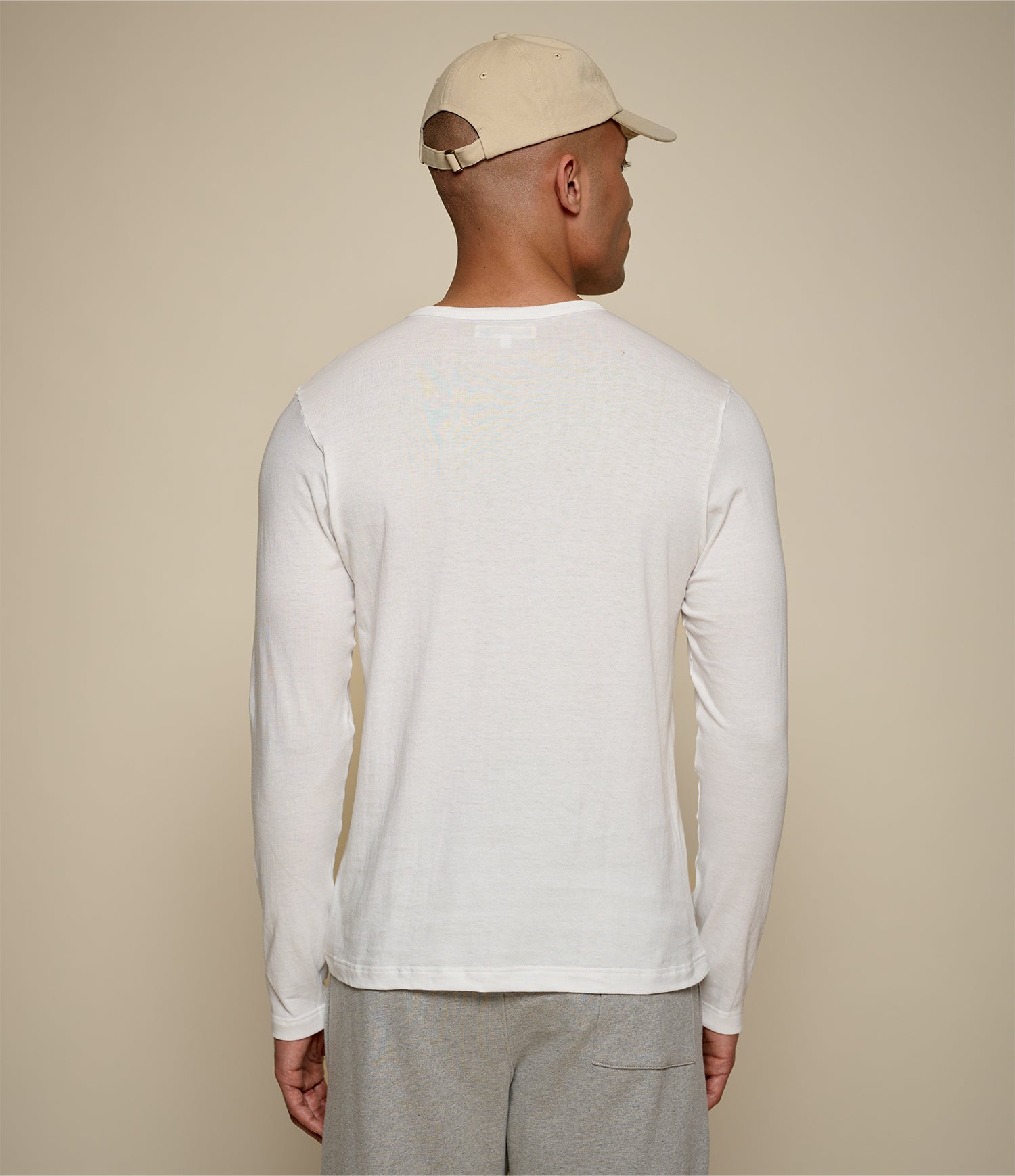 Man wearing a white loopwheeled long-sleeve shirt and beige cap against a beige background