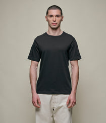 Man wearing a black t-shirt and beige pants against a plain background