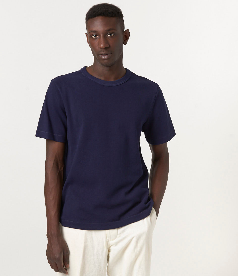 A person wearing a navy blue loopwheeled pikée T-shirt with a relaxed fit and short sleeves.