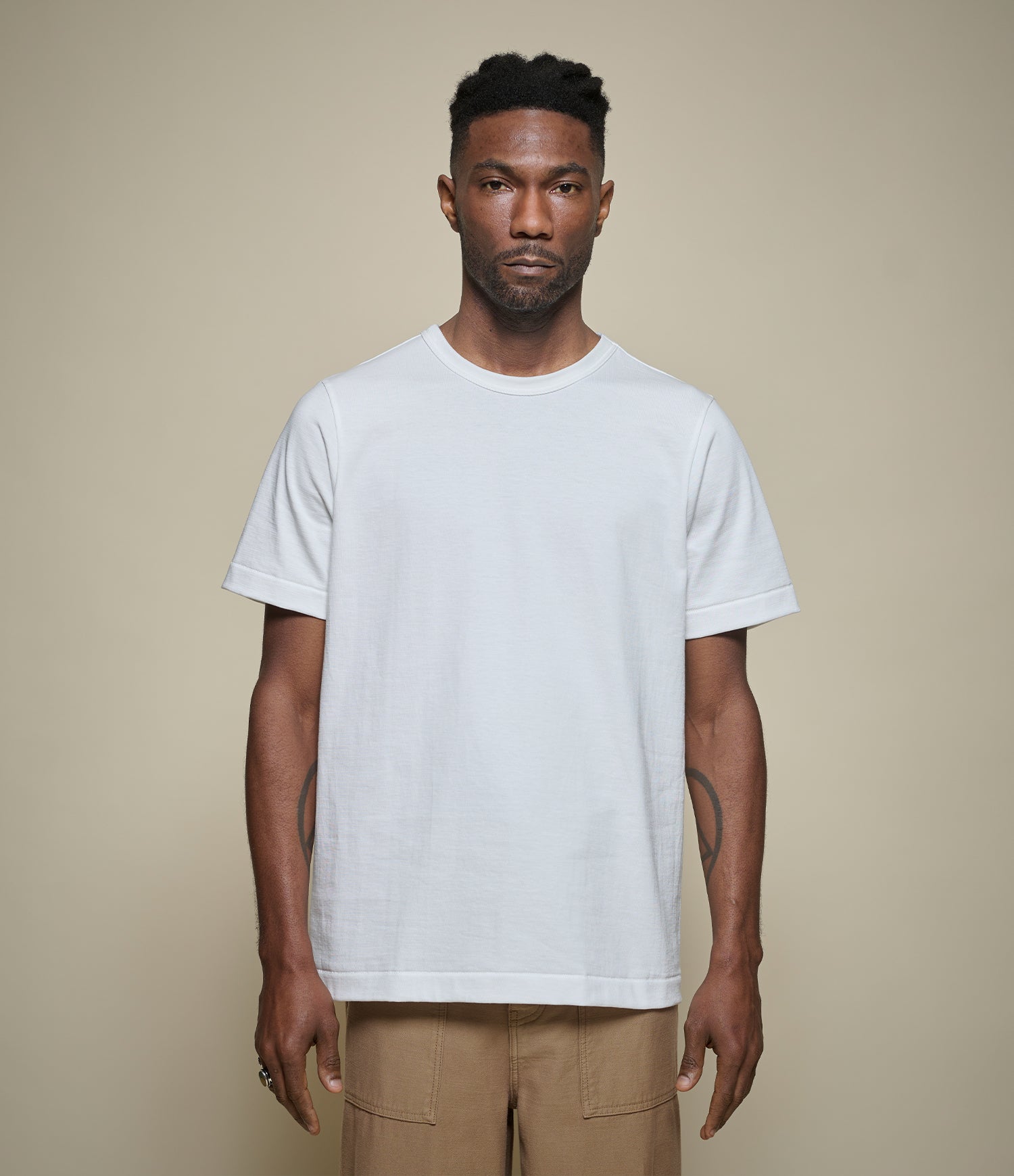 Man wearing a plain white relaxed fit loopwheeled t-shirt against a beige background