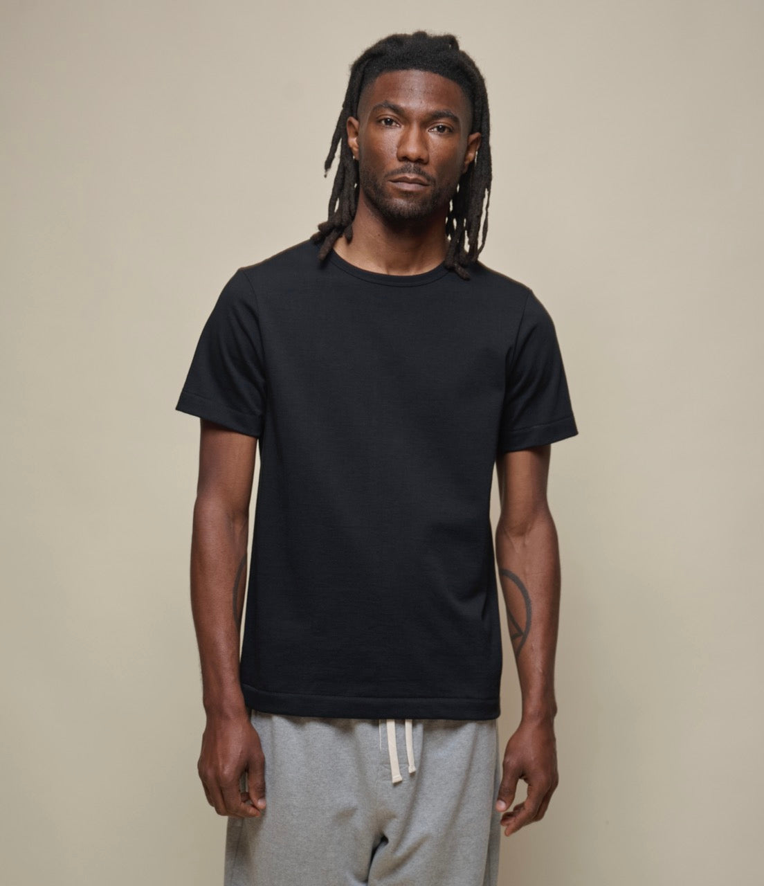 A person wearing a black  loopwheeled, short-sleeved T-shirt with a round neck, paired with light-colored pants.