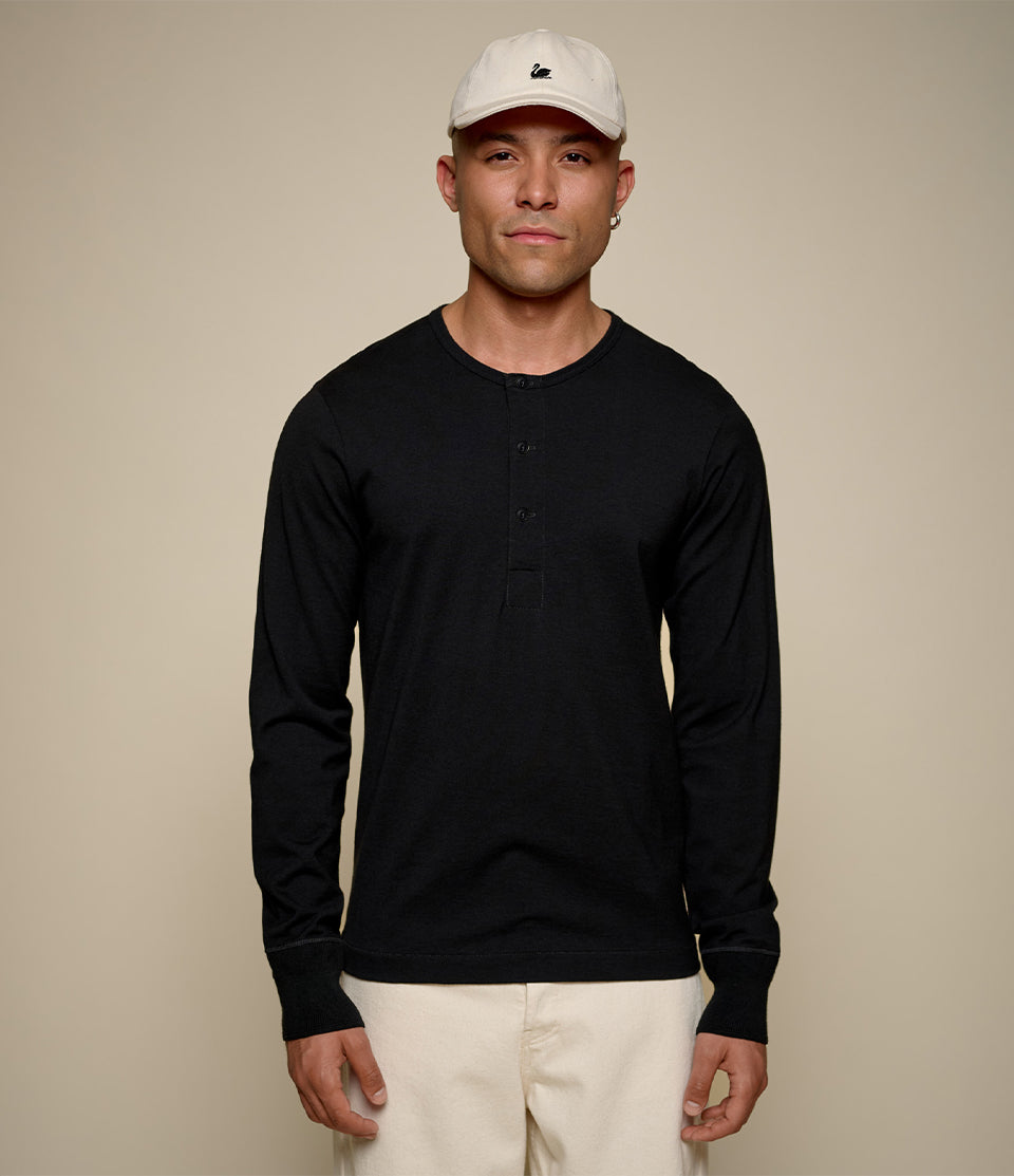 Man wearing a black long-sleeve henley shirt and beige cap against a beige background