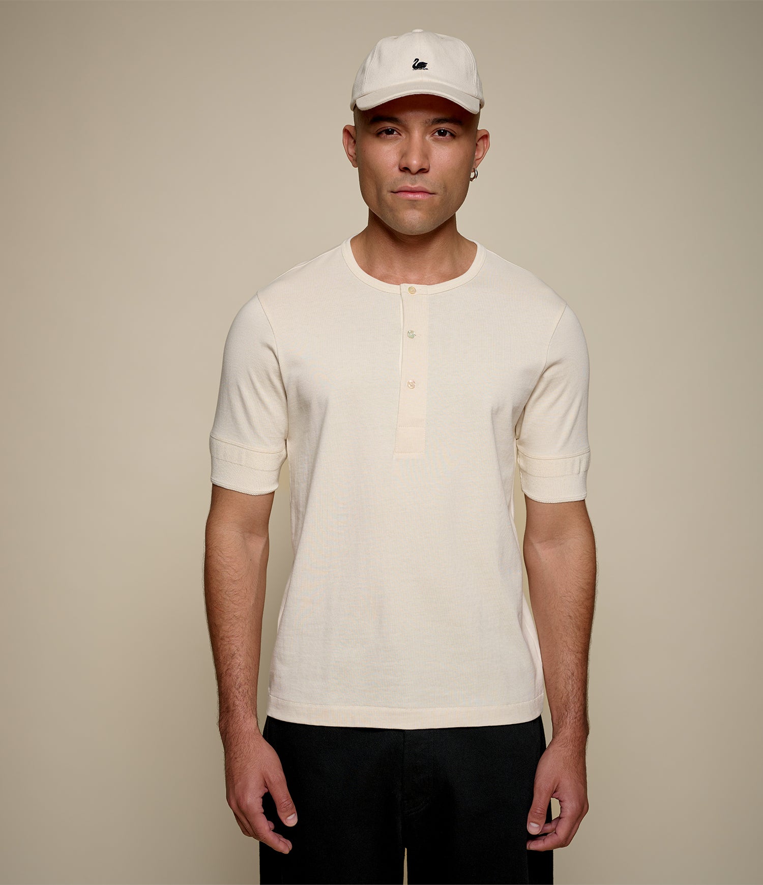Man wearing a beige henley shirt and white cap against a beige background