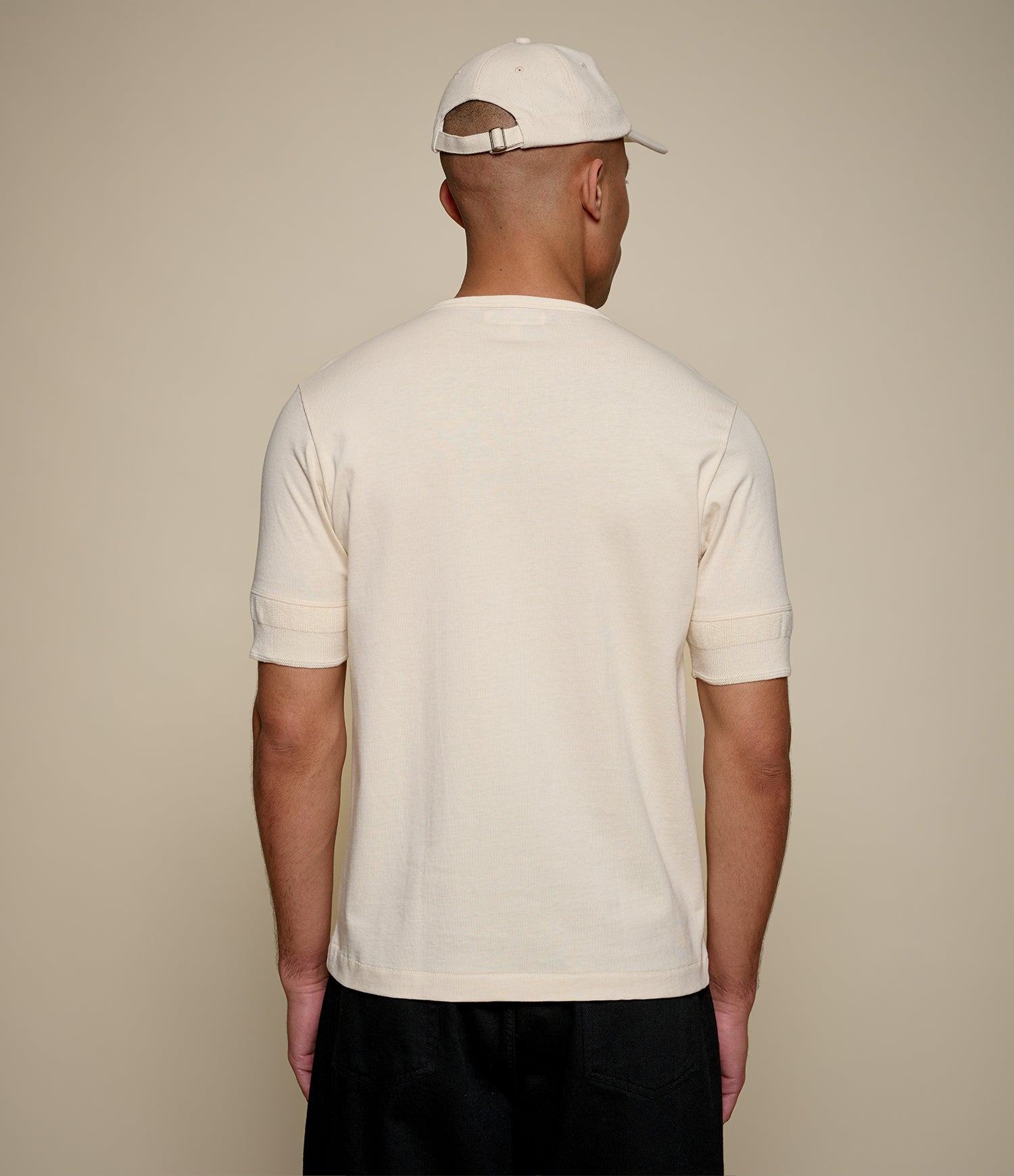 Man wearing a beige henley shirt and beige cap against a beige background