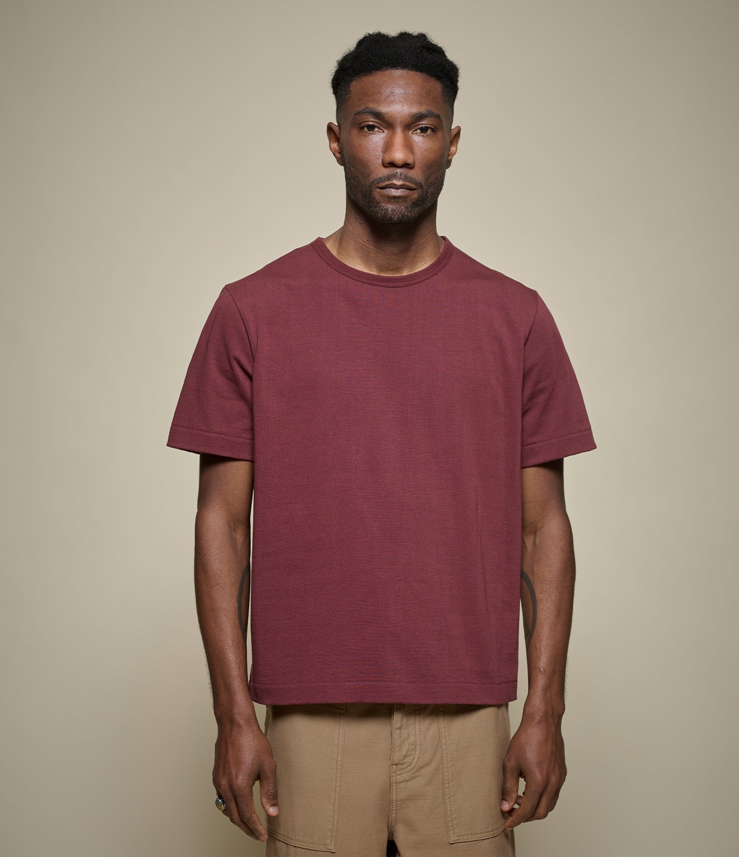 Man wearing a burgundy cropped t-shirt against a beige background