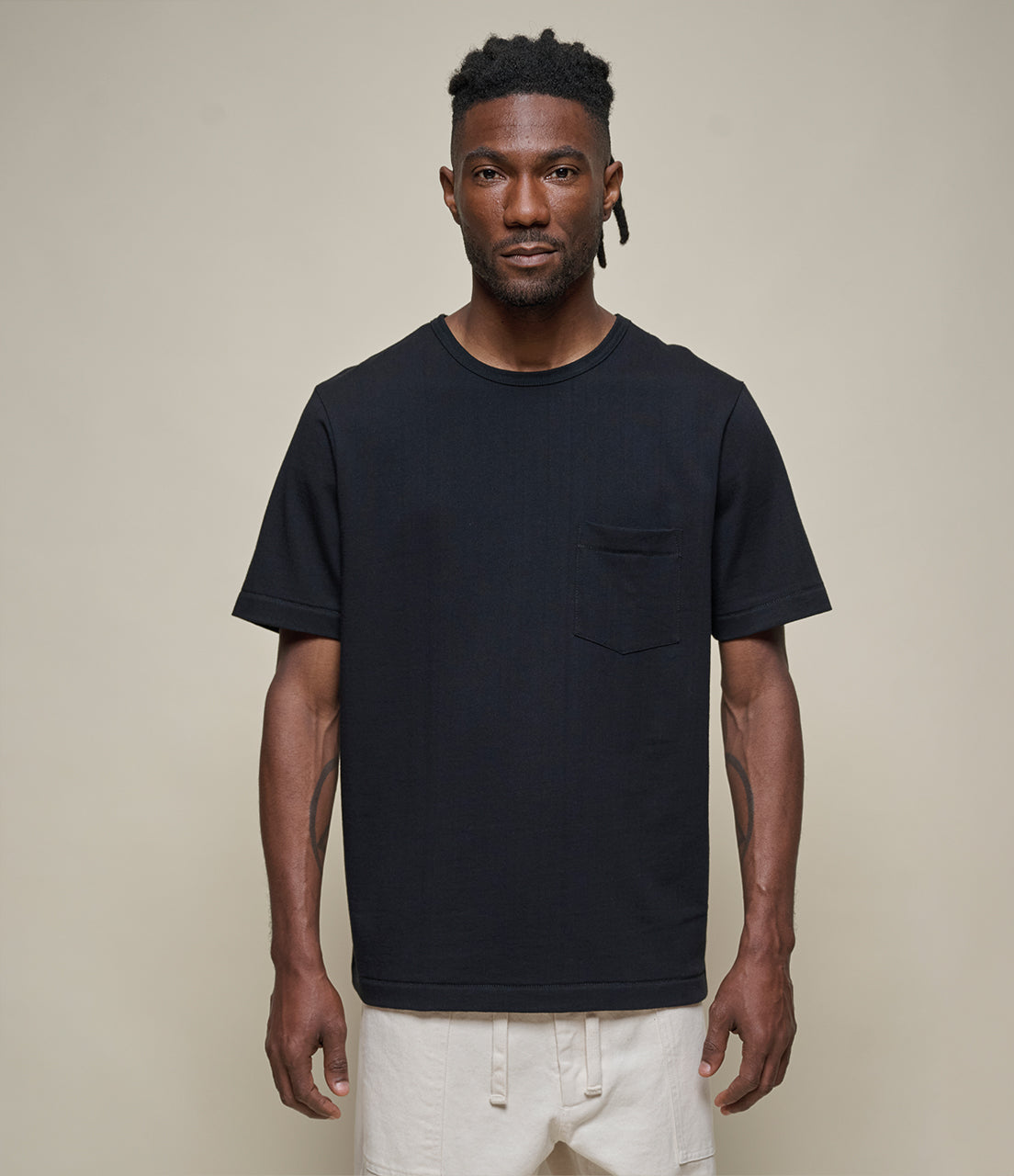 Man wearing a black t-shirt with a pocket on a beige background