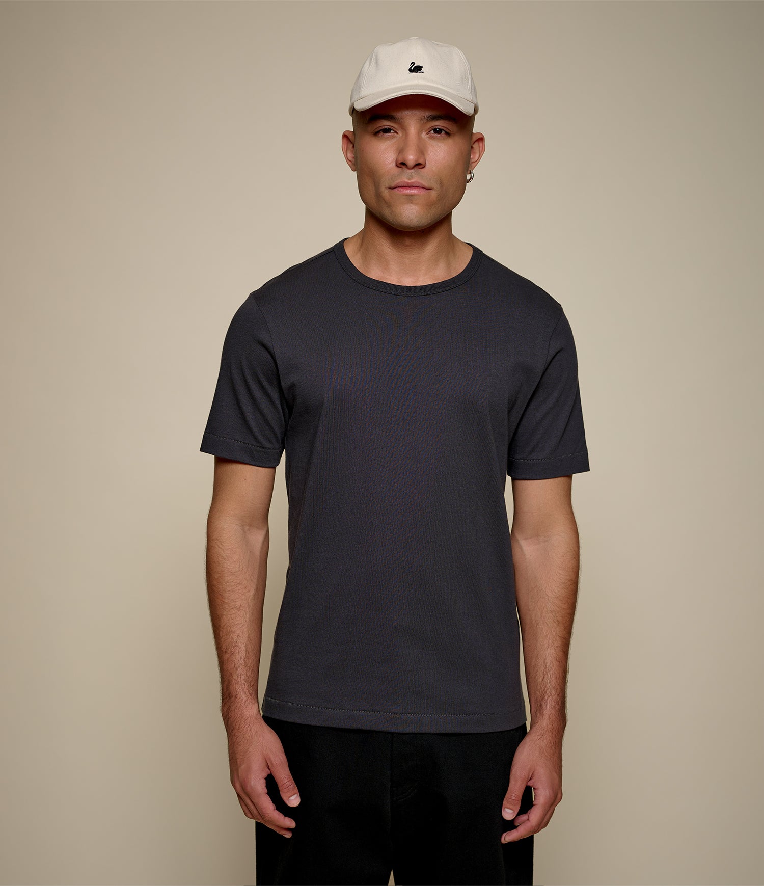 Man wearing a dark gray t-shirt and white cap against a beige background