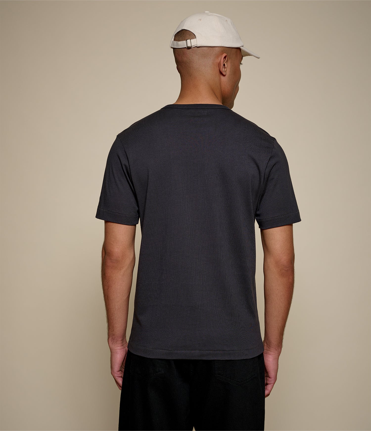 Man wearing a dark grey t-shirt and beige cap on a beige background