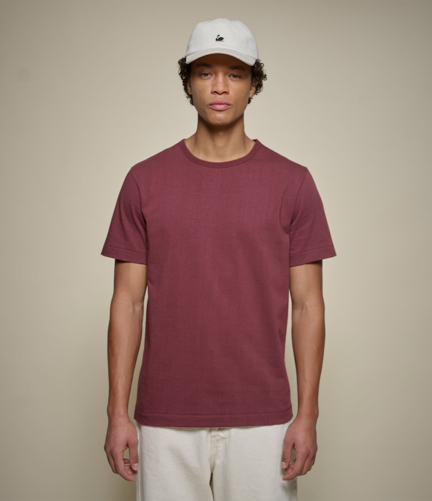 Person wearing a maroon t-shirt and white cap against a beige background