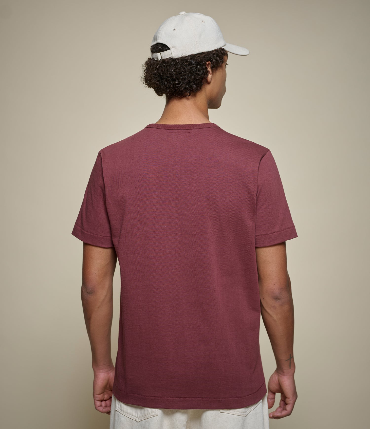 Person wearing a maroon t-shirt and white cap from behind on a beige background