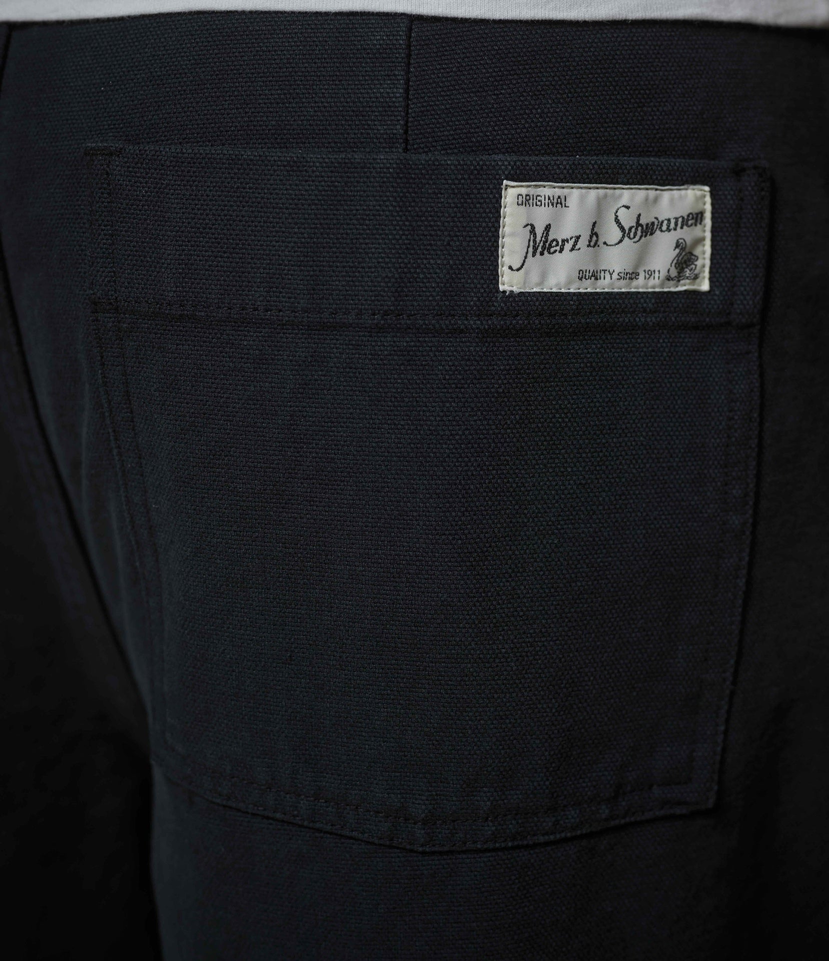Close-up of the back pocket of black denim jeans, showing a white woven brand label that reads 'Merz b. Schwanen'.