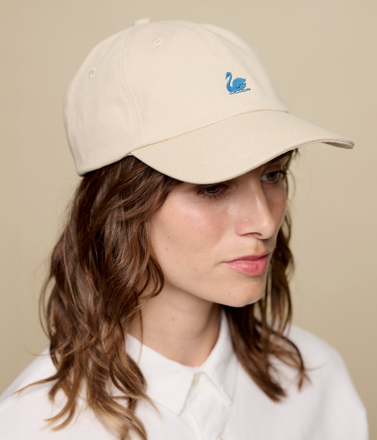 Person wearing a beige cap with a logo on a beige background