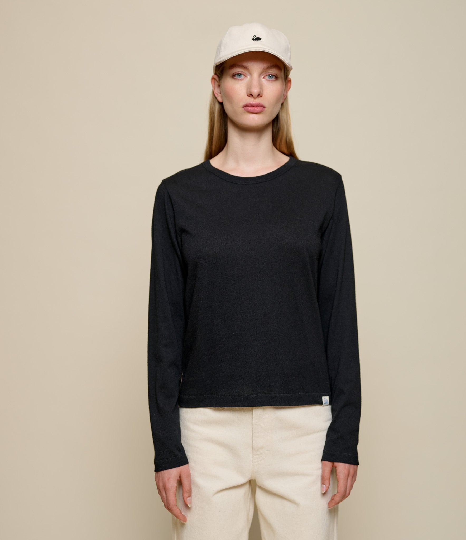 Person wearing a black long-sleeve cashmere shirt and white cap on a beige background