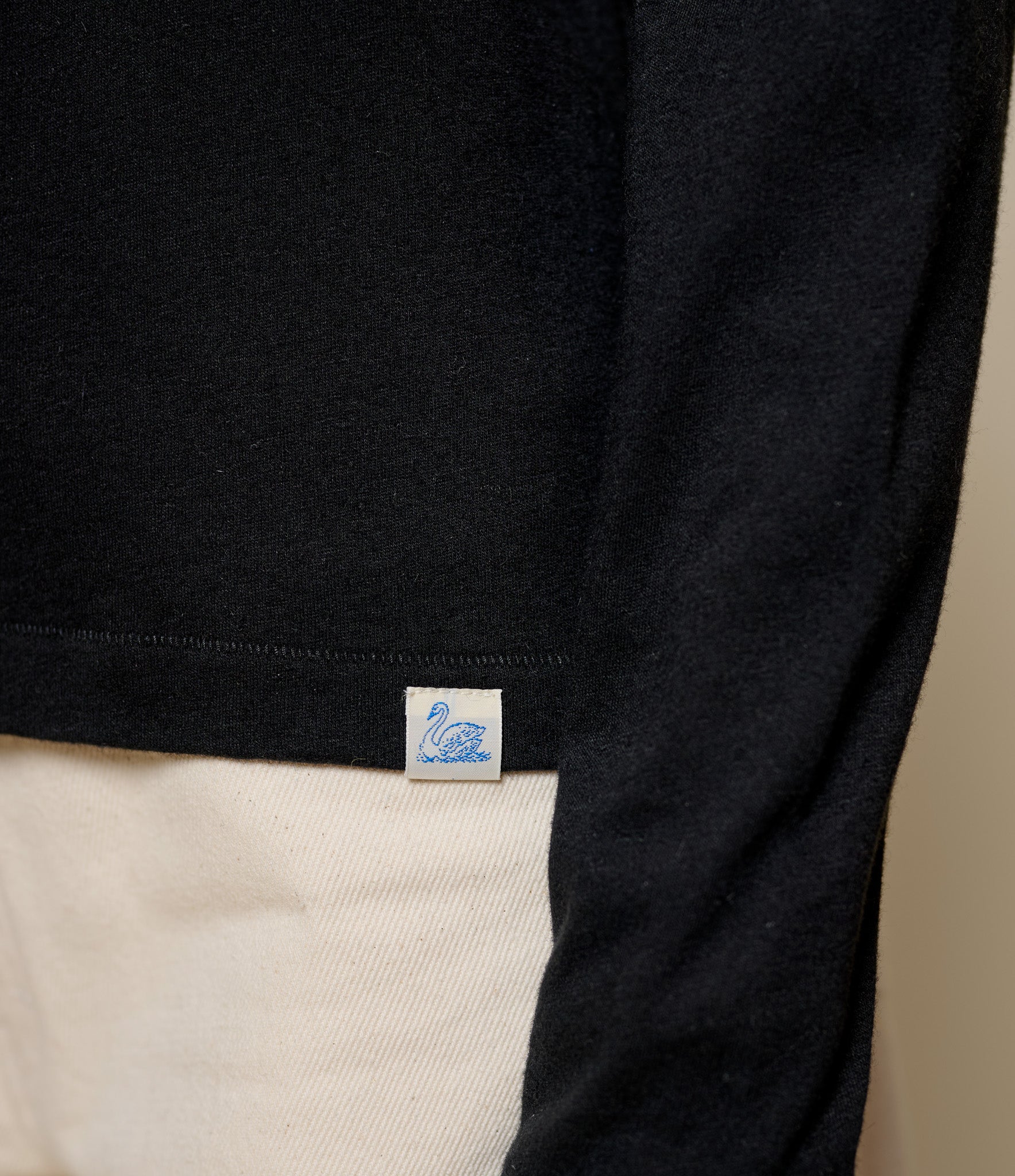 Close-up of black long-sleeve cashmere shirt with a swan logo label on a beige background