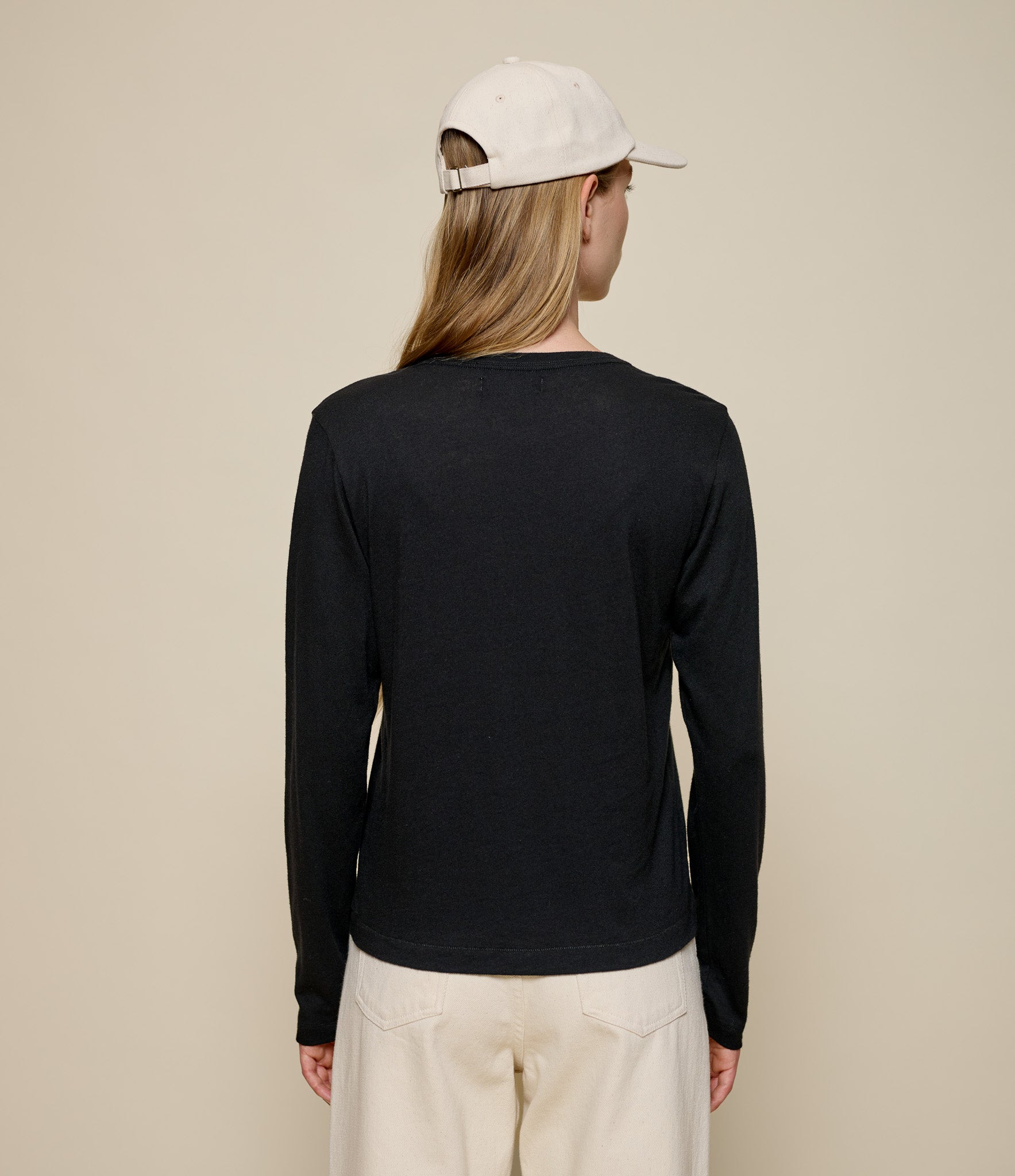 Person wearing a black long-sleeve cashmereshirt and beige cap on a beige background