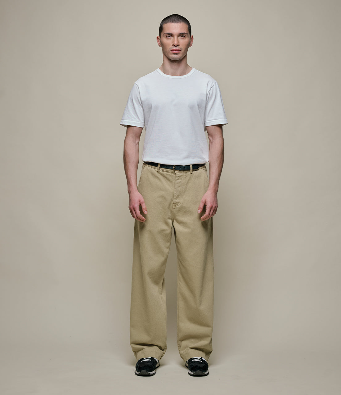 Man wearing a white t-shirt and beige pants against a plain background
