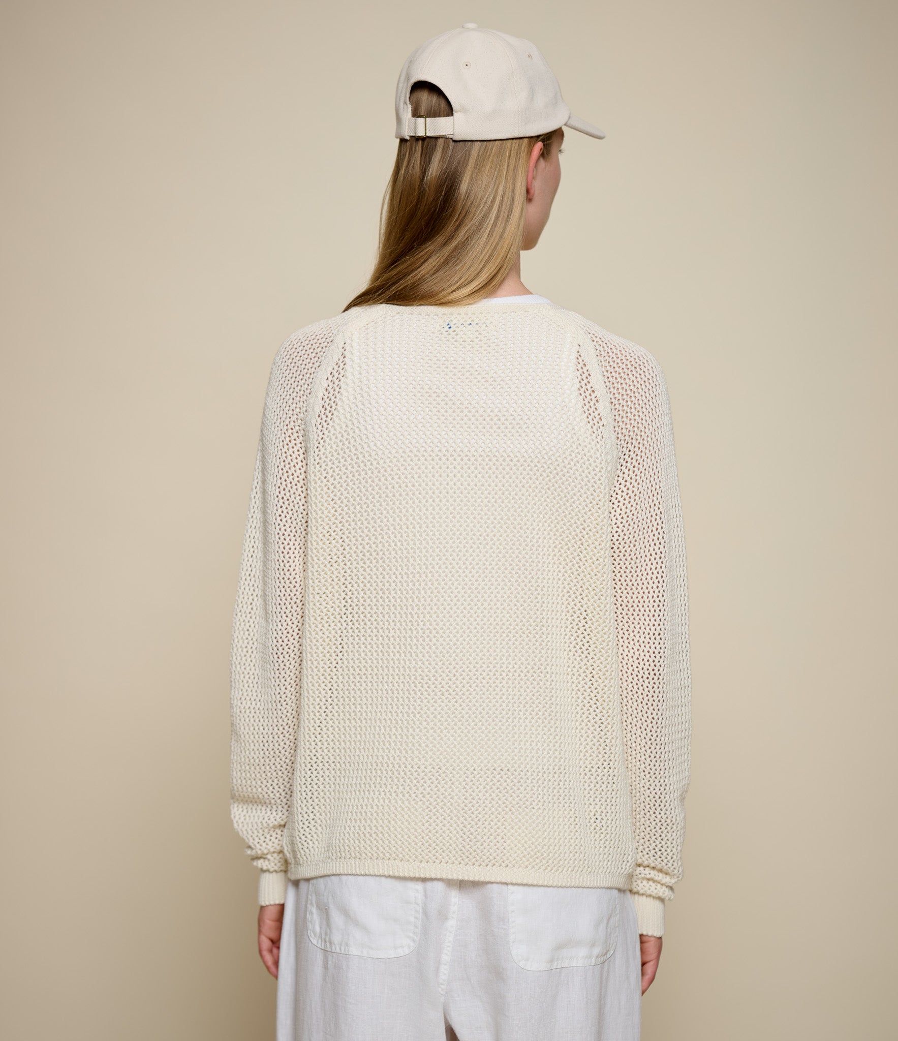 Person wearing a beige knitted crochet sweater and cap on a beige background