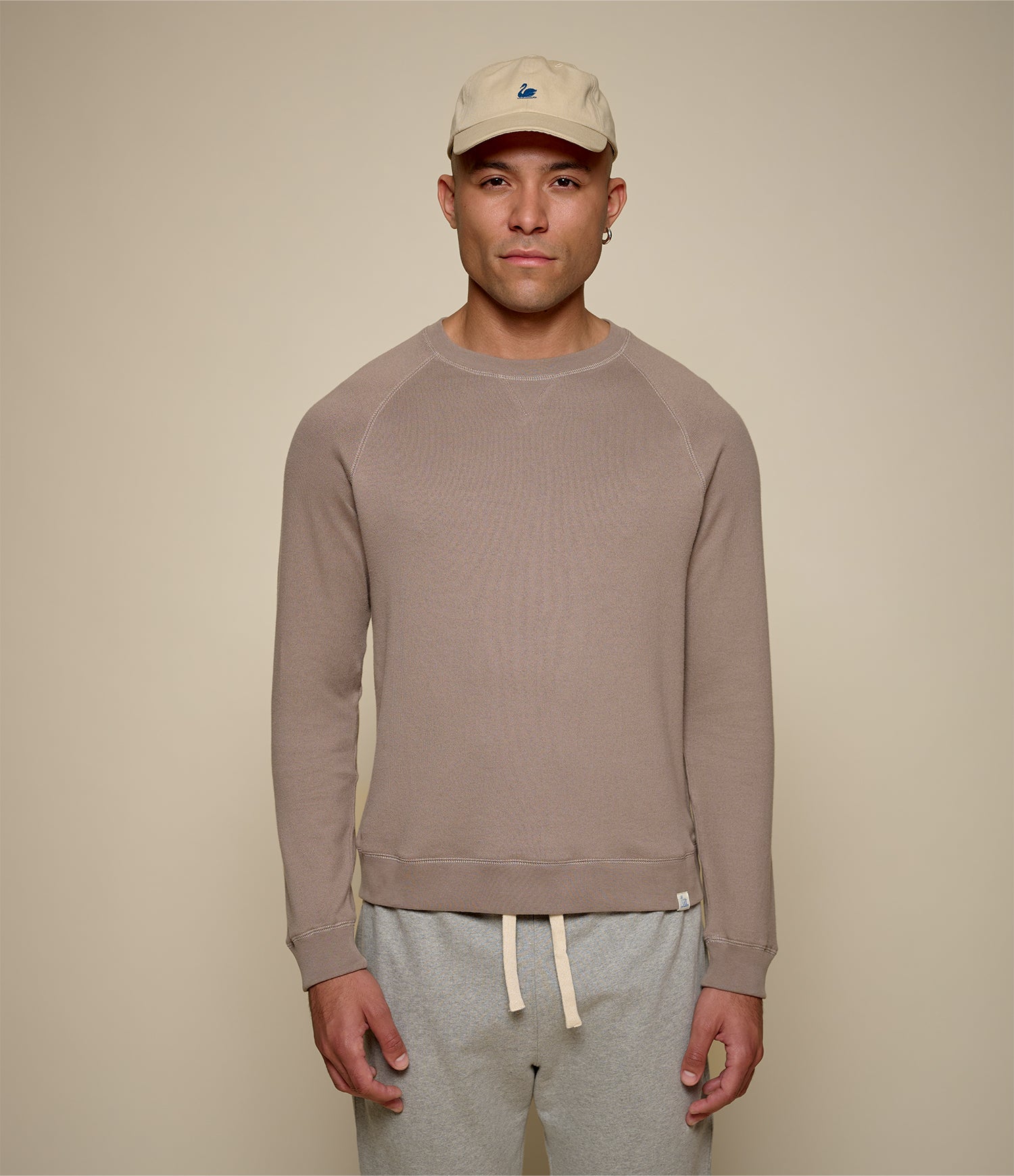 Man wearing a beige cap and brown sweatshirt against a beige background