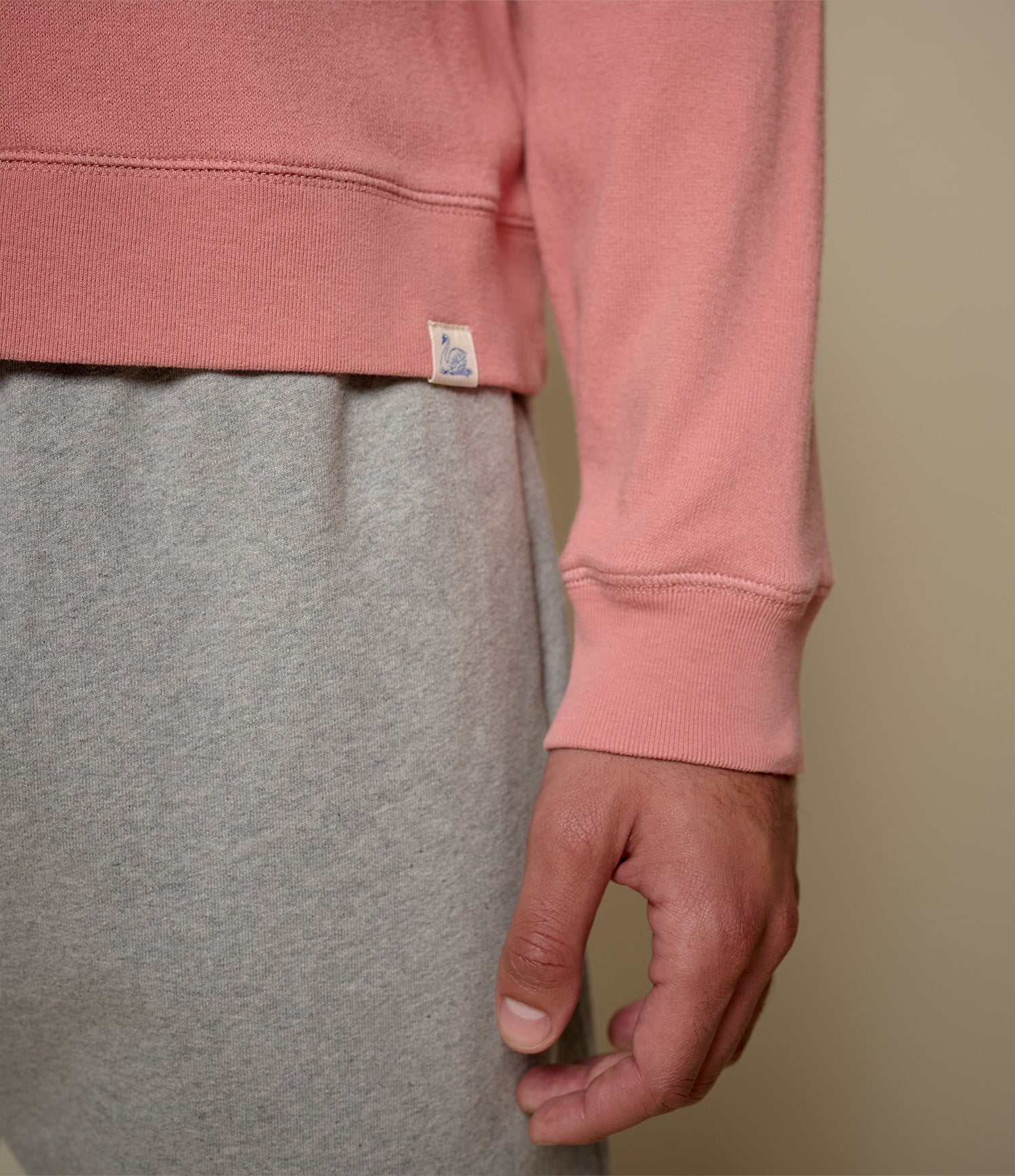 Person wearing a pink sweatshirt and gray pants with a beige background