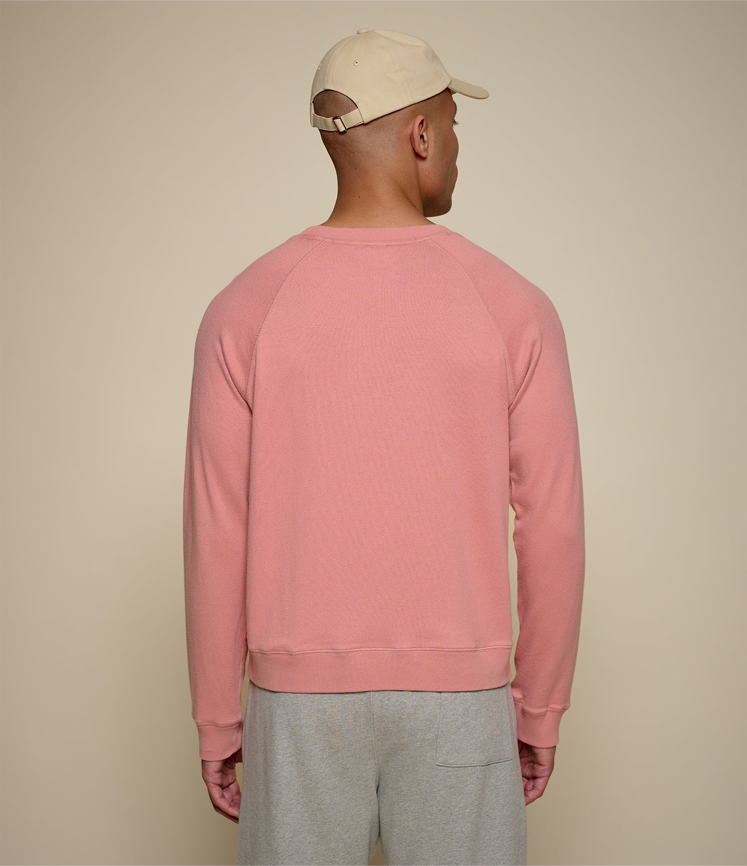 Man wearing a pink sweatshirt and beige cap on a beige background