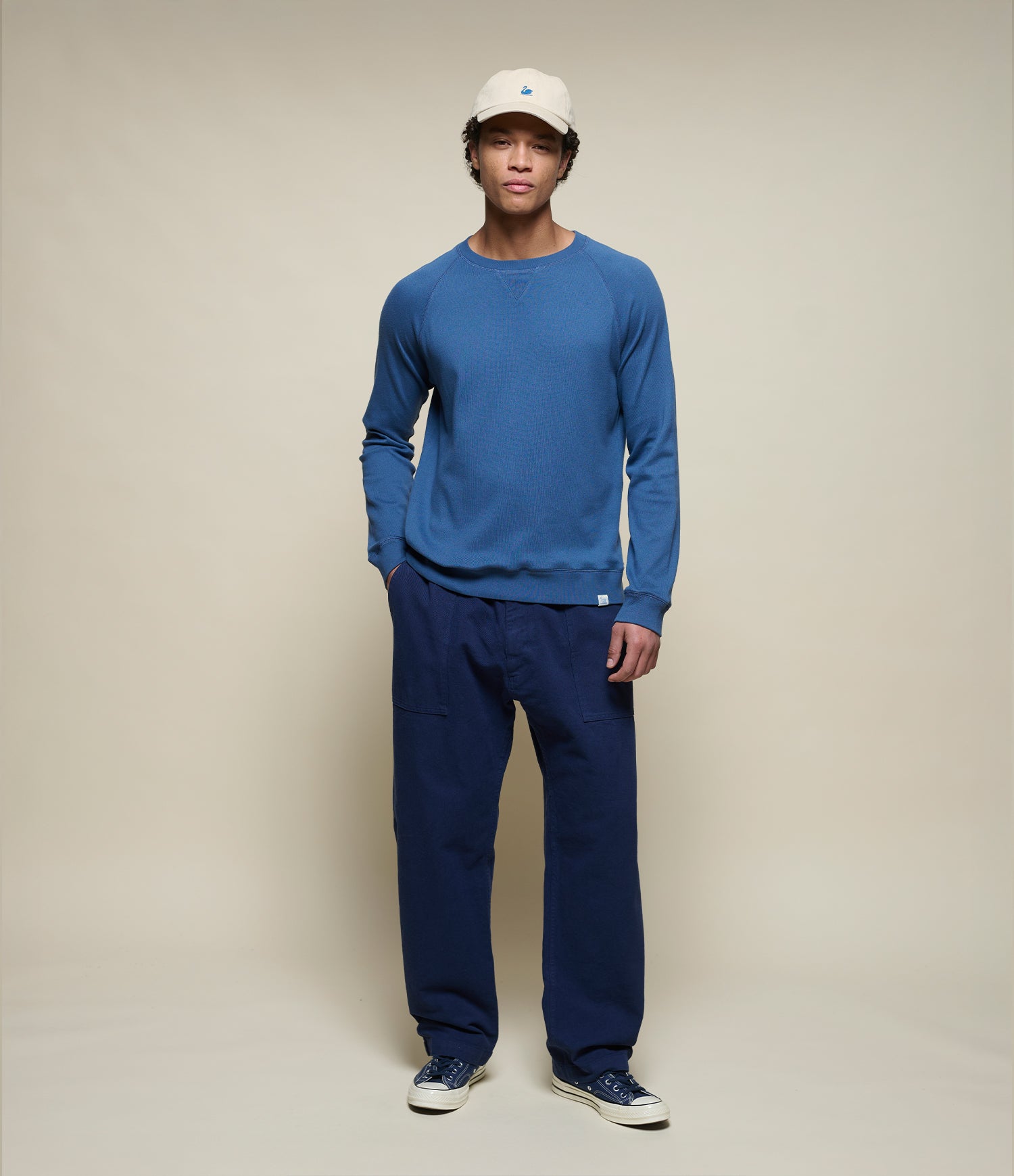 Person wearing aan indigo blue lightweight sweatshirt and dark blue pants on a beige background