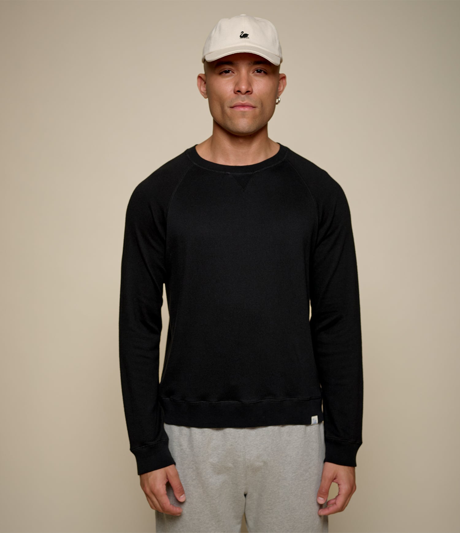 Man wearing a black sweatshirt and gray pants against a beige background