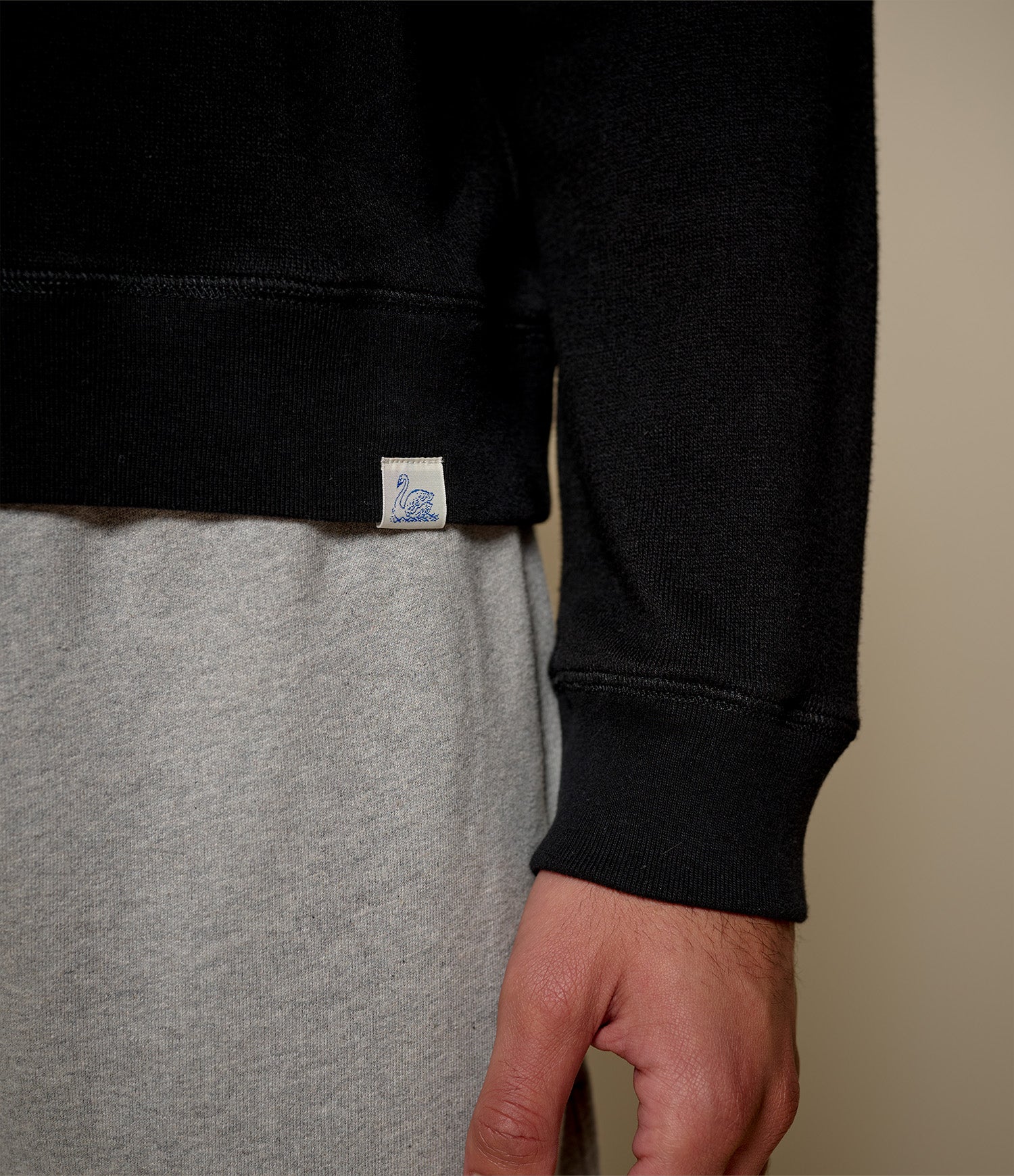 Person wearing a black sweatshirt with a visible brand label on a beige background
