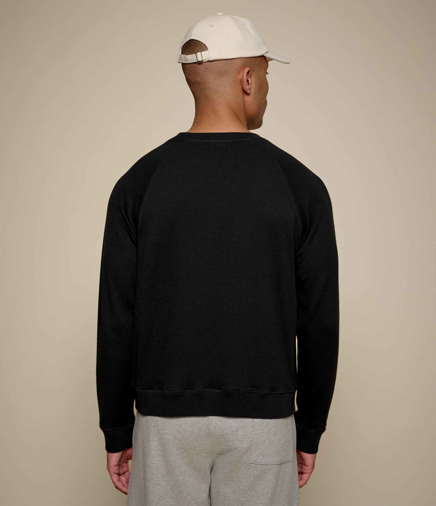Man wearing a black sweatshirt and gray pants with a beige cap on a beige background