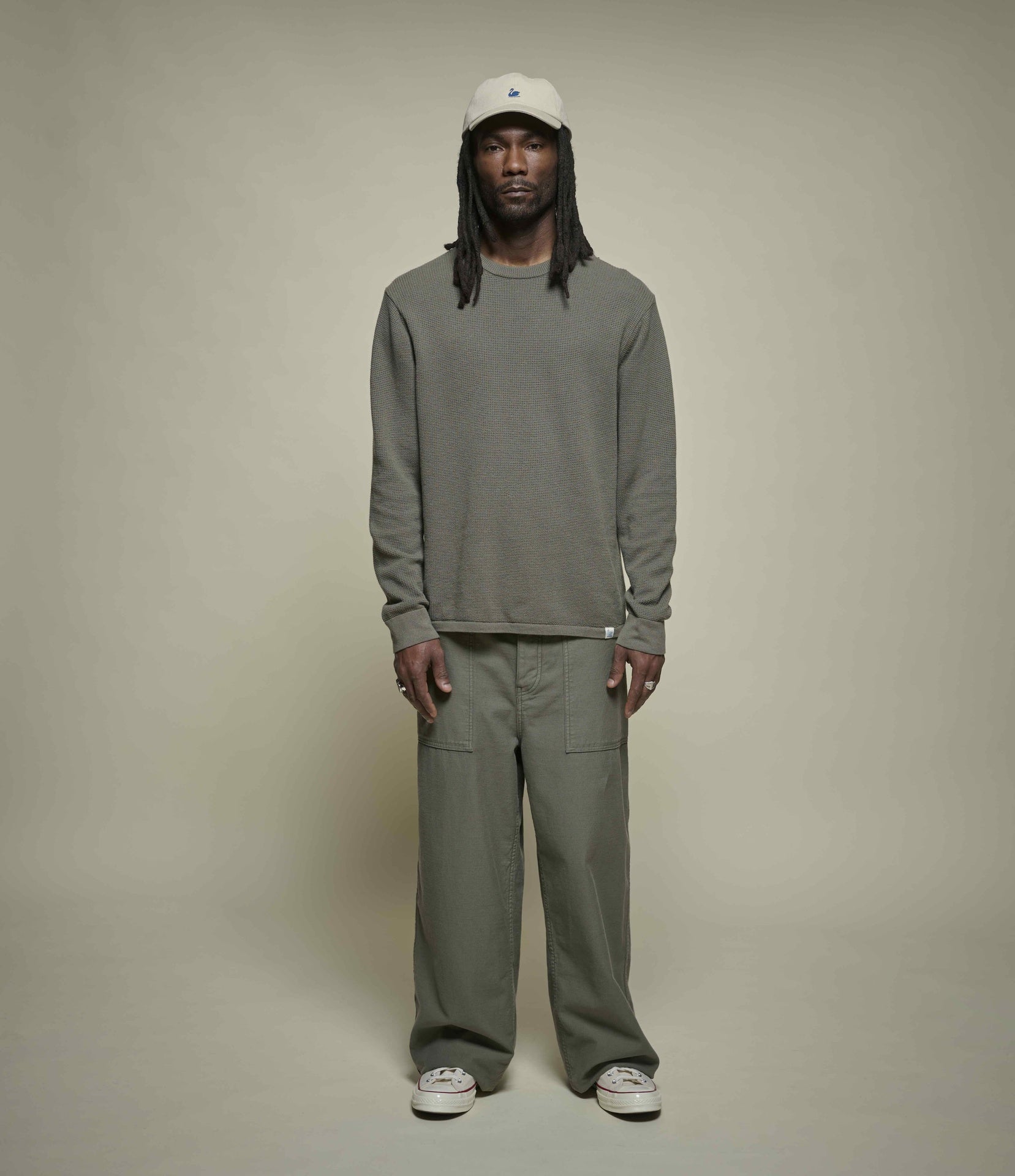 Person wearing a lightweight textured sweater and pants with a white cap on a beige background