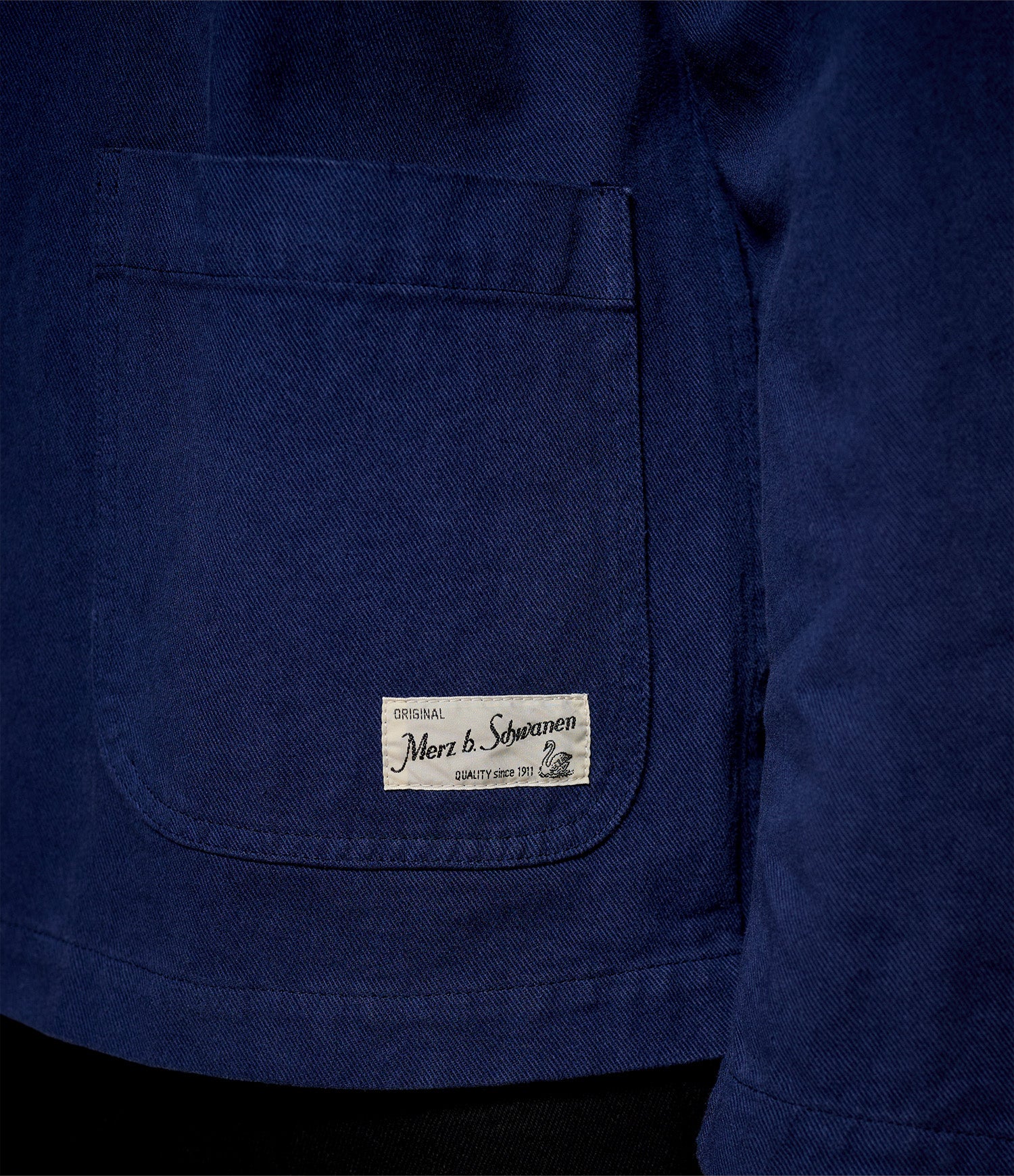 Close-up of a blue twill jacket with Merz b. Schwanen brand label on the chest pocket.