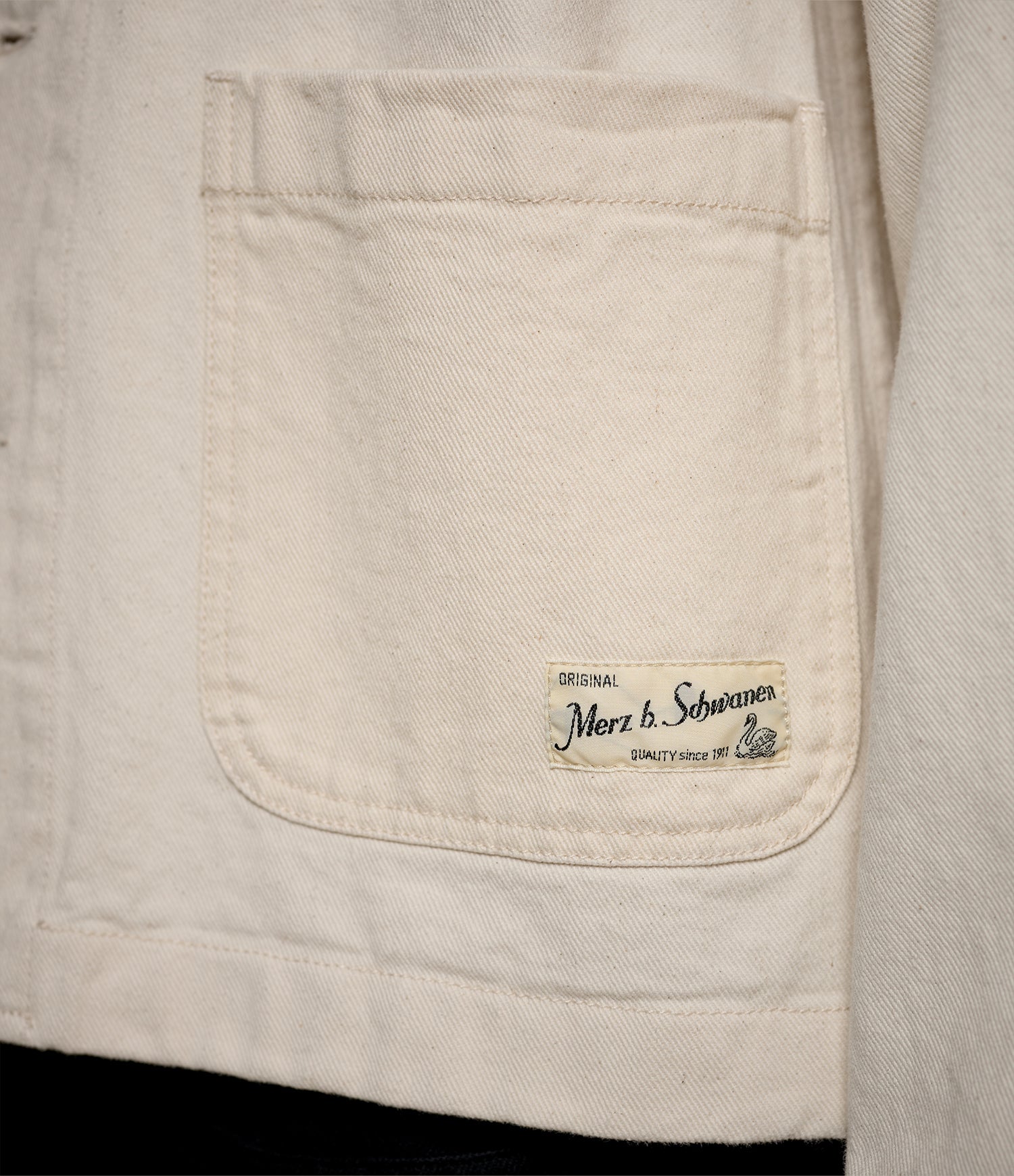 Close-up of a beige twill jacket pocket with a Merz b. Schwanen label on a light background