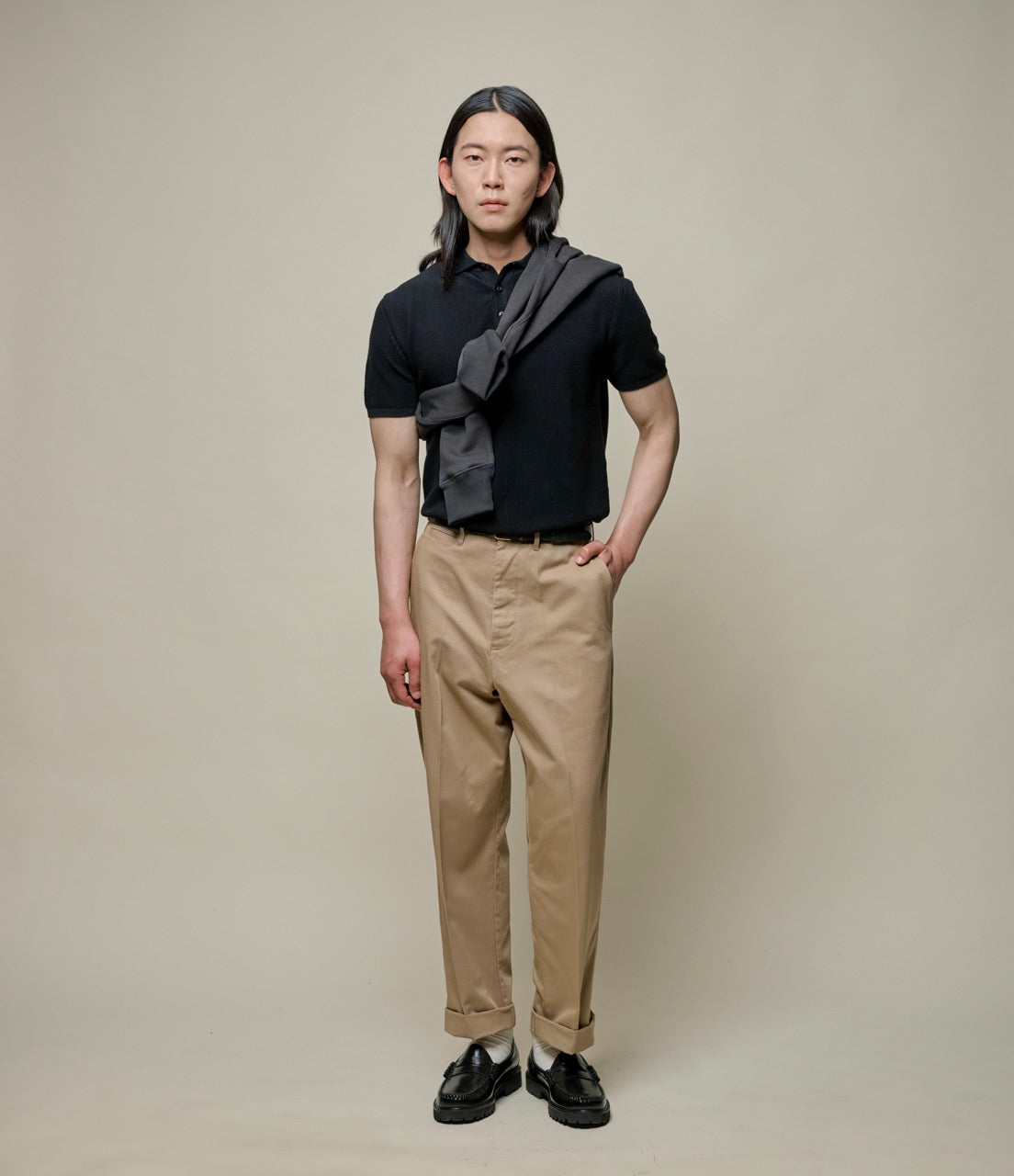 Person wearing a black polo shirt and beige pants with a gray scarf.