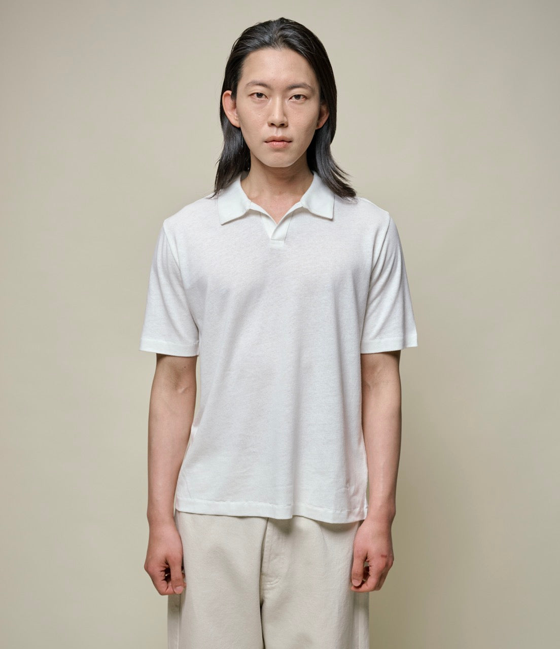 Person wearing a white linen polo shirt against a plain background