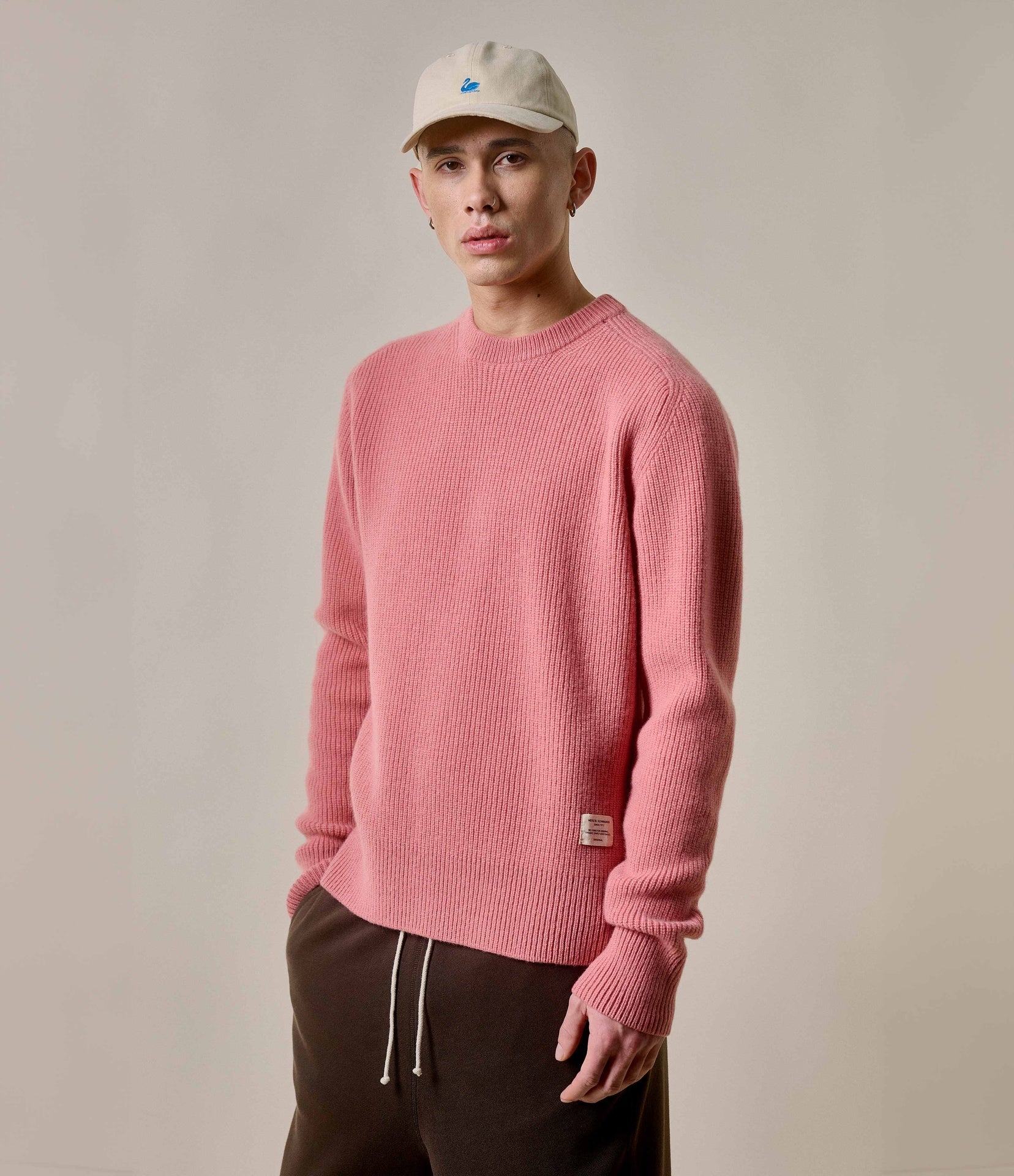 Man wearing a pink sweater and beige cap against a plain background