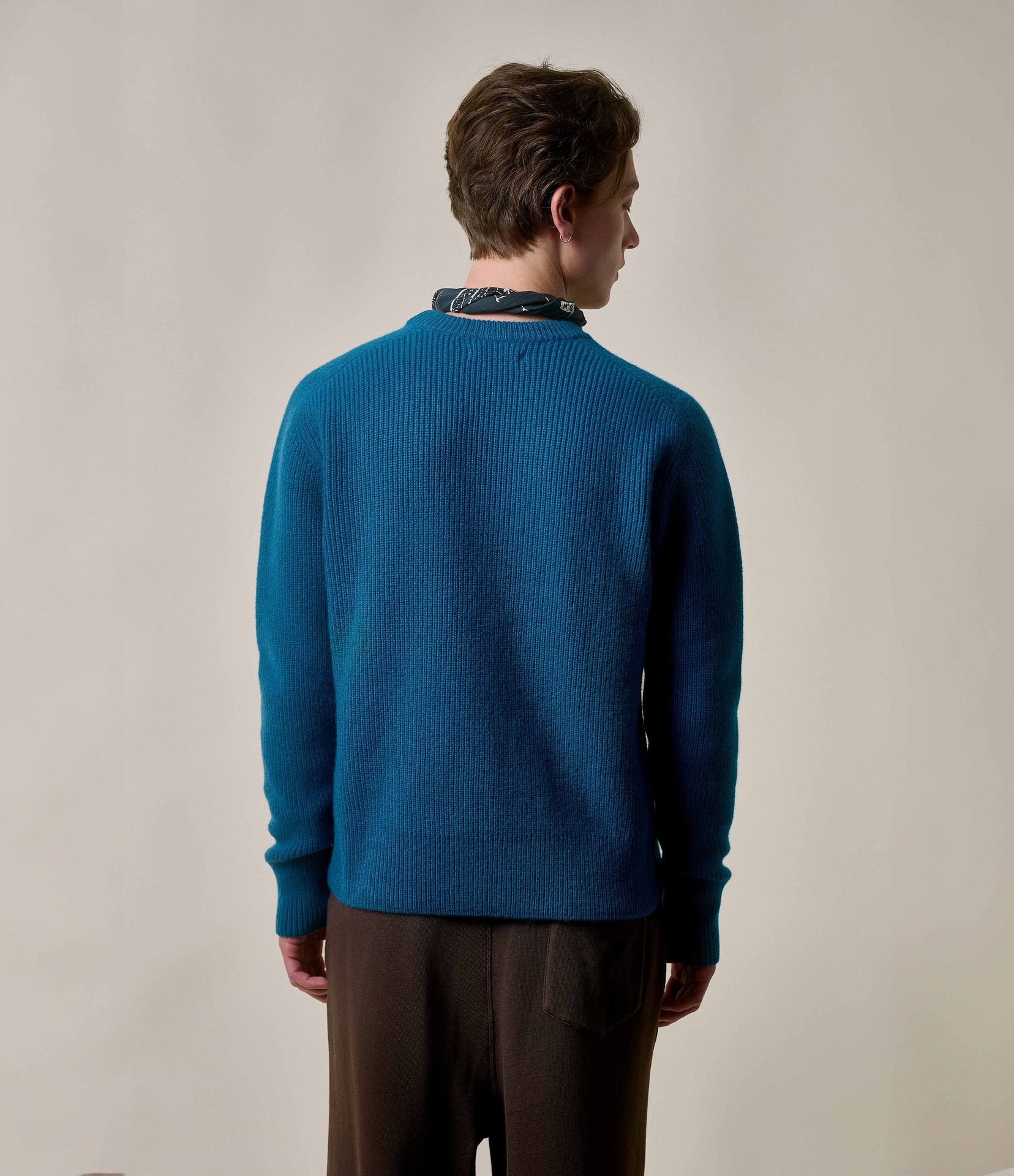 Person wearing a blue sweater and brown pants against a plain background