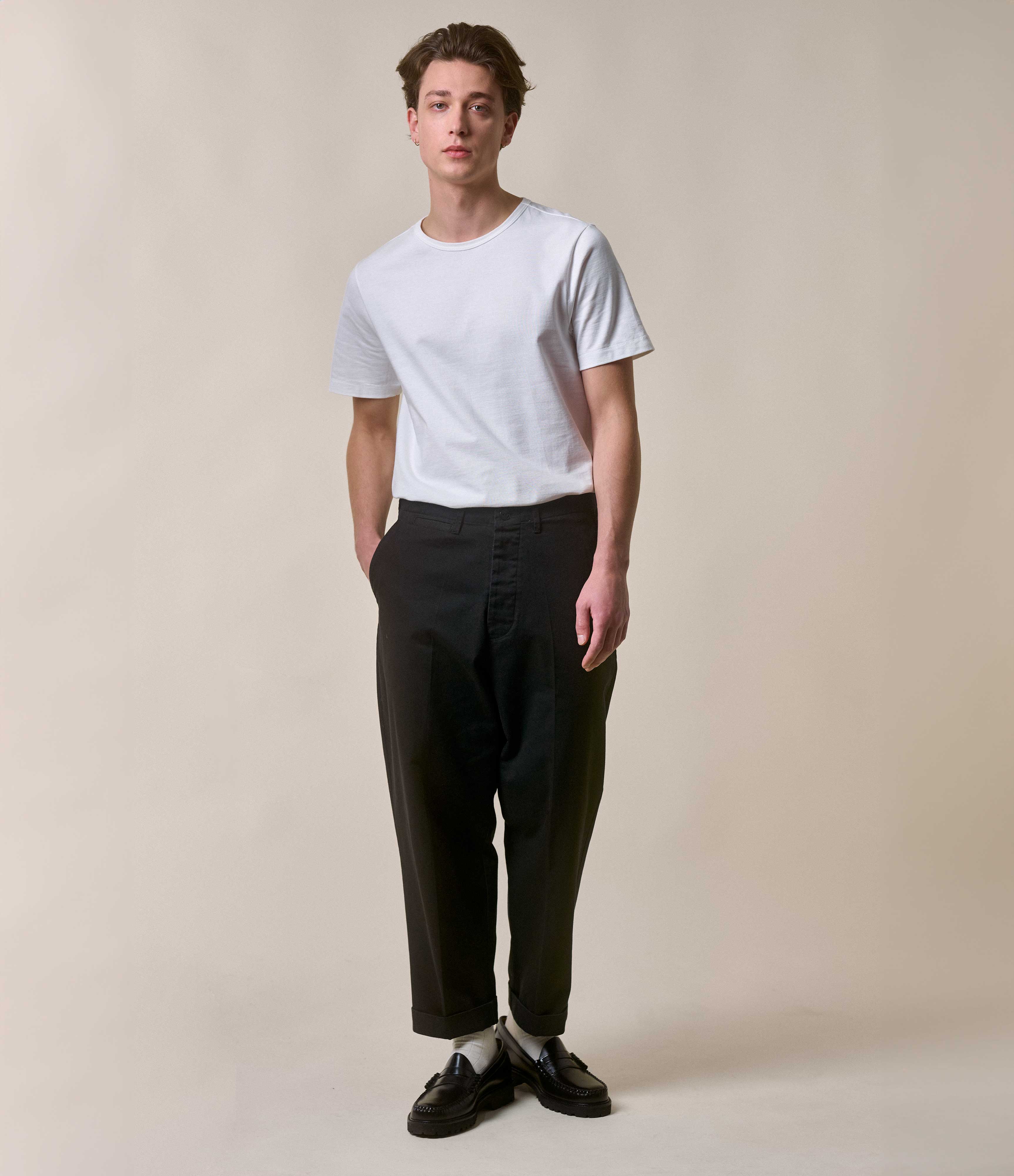 Man wearing a white t-shirt and black pants against a beige background