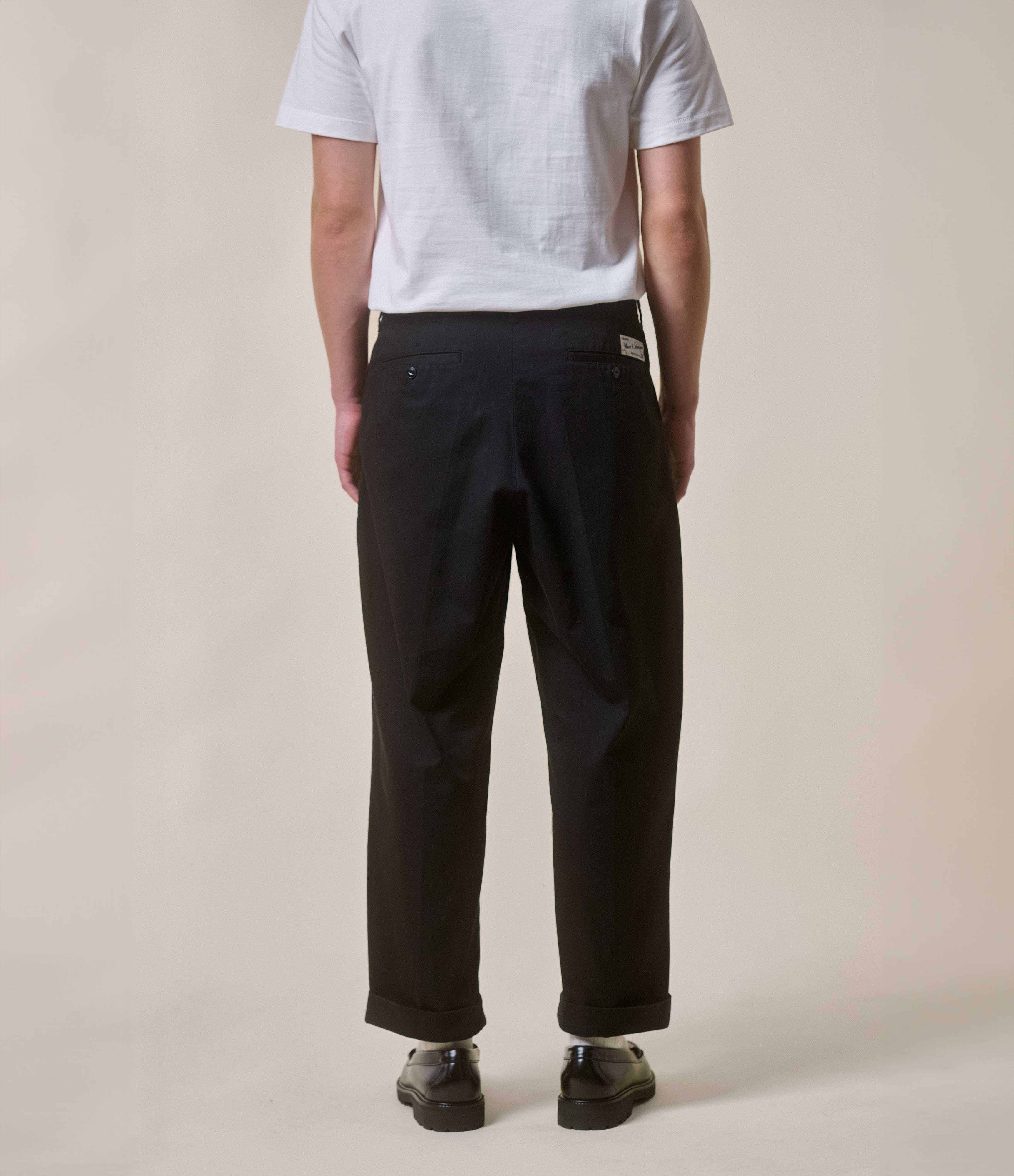 Person wearing black chinos and a light gray shirt on a beige background