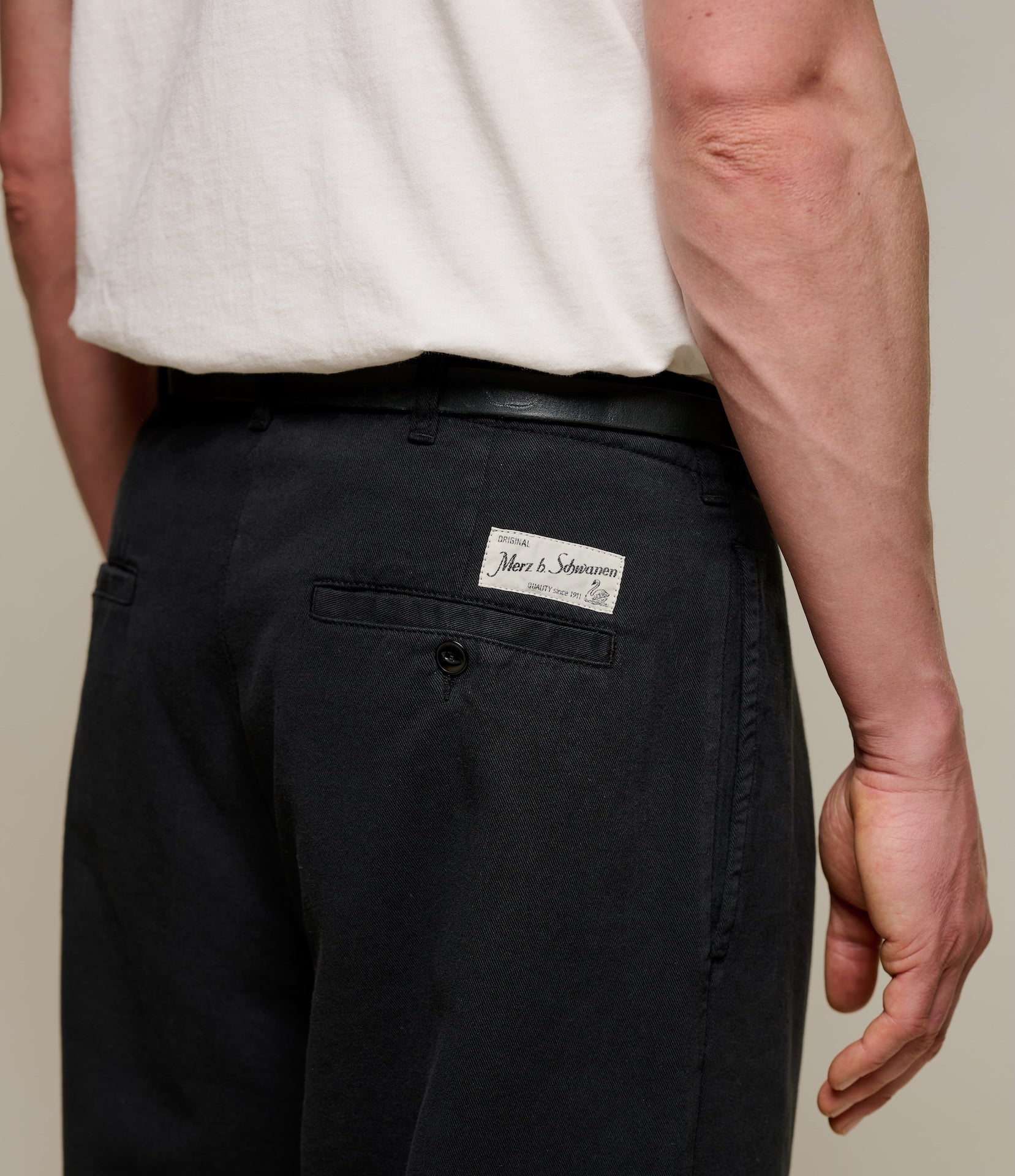 Person wearing black pants with a Merz b. Schwanen brand label on a neutral background