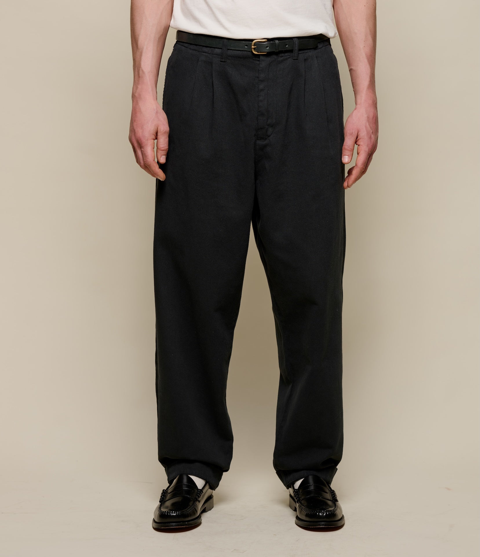 Person wearing black pleated pants and a white shirt against a beige background