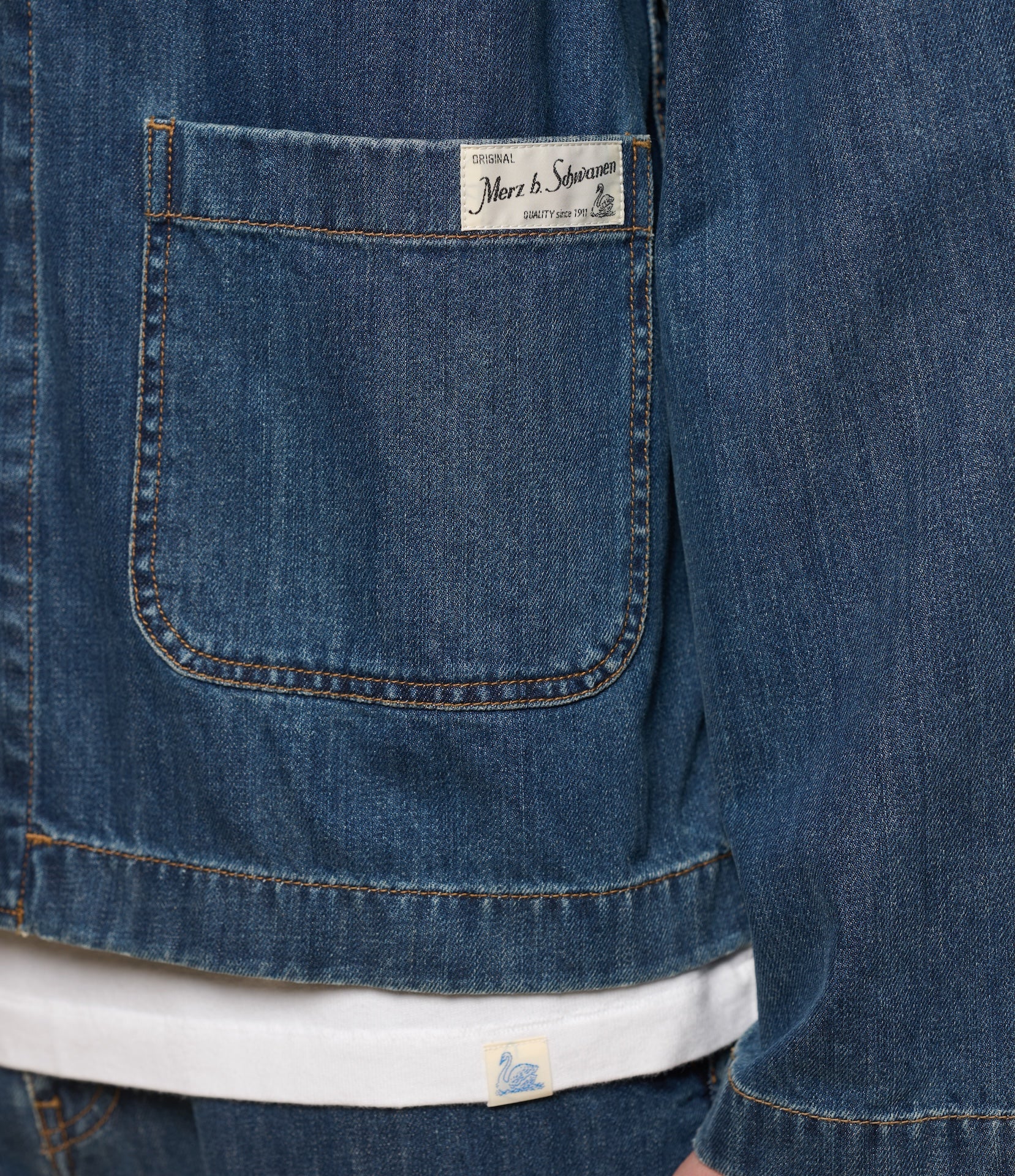 Close-up of a blue denim shirt with a Merz b. Schwanen brand label on the front pocket.