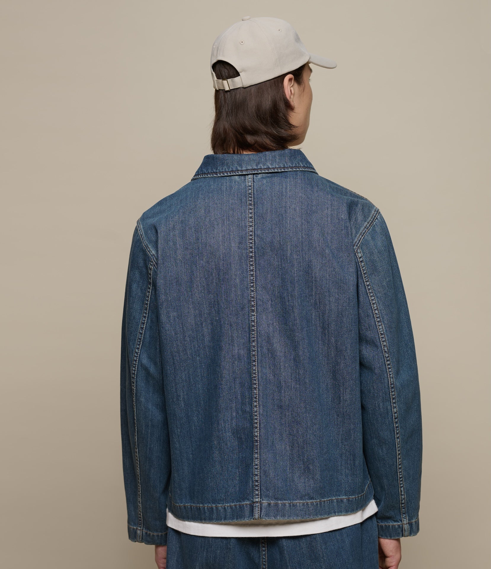Person wearing a blue denim jacket and beige cap on a beige background