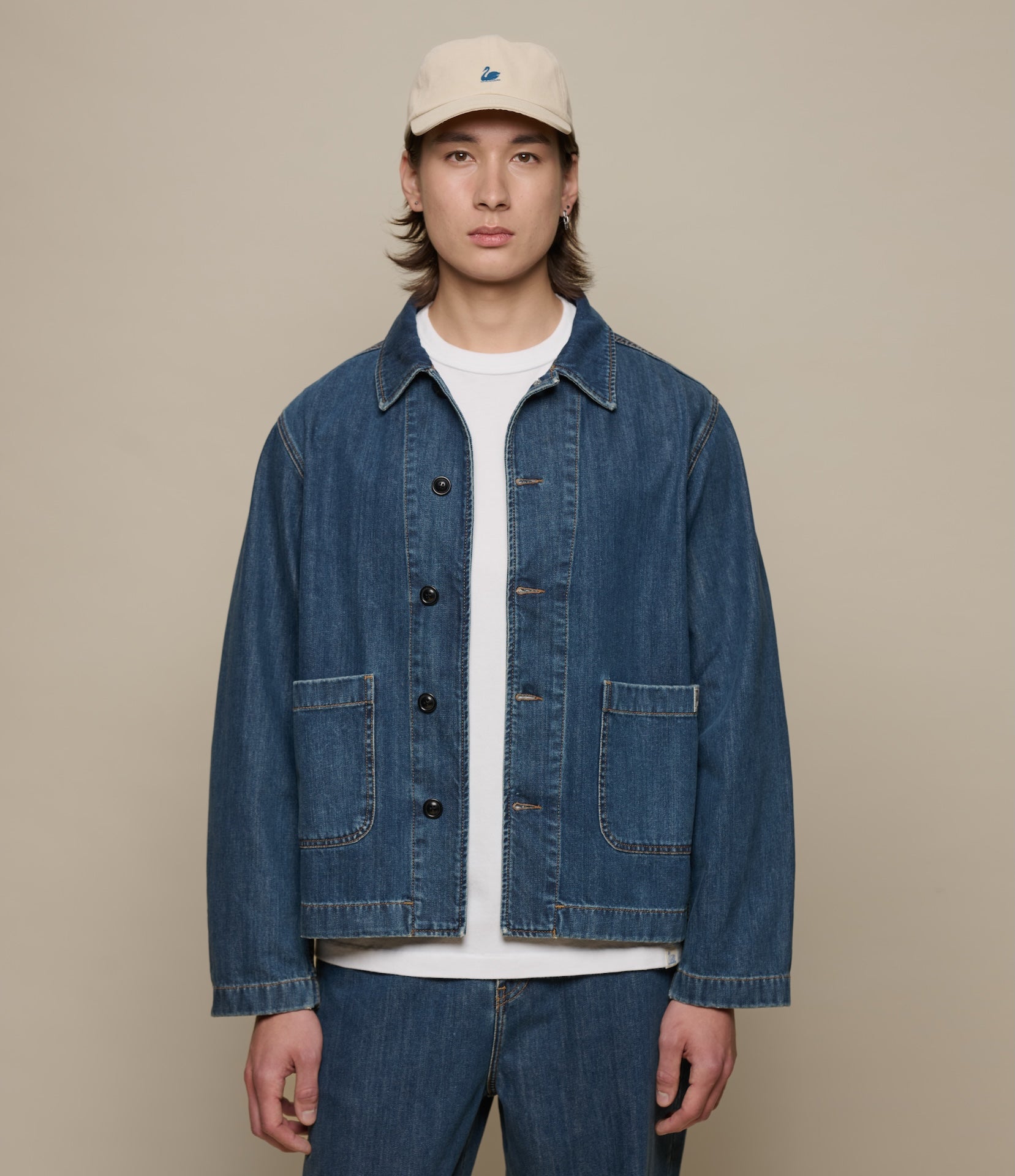 Man wearing a cropped blue denim jacket and beige cap on a beige background