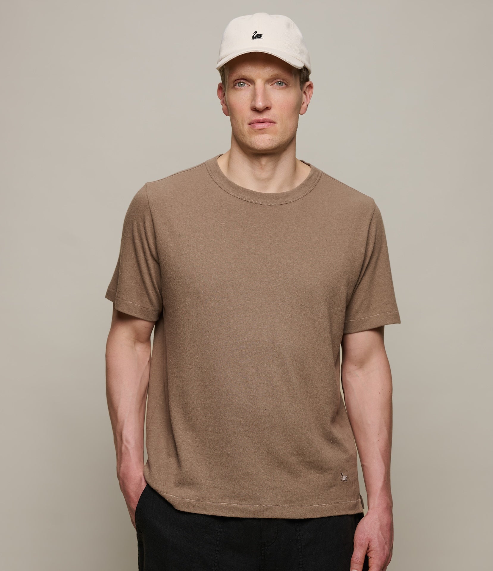 Man wearing a brown linen t-shirt and beige cap against a plain background