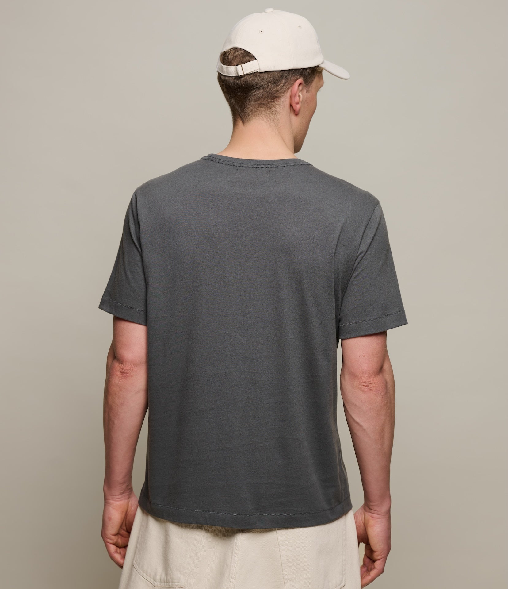 Man wearing a gray t-shirt and beige cap from behind on a plain background