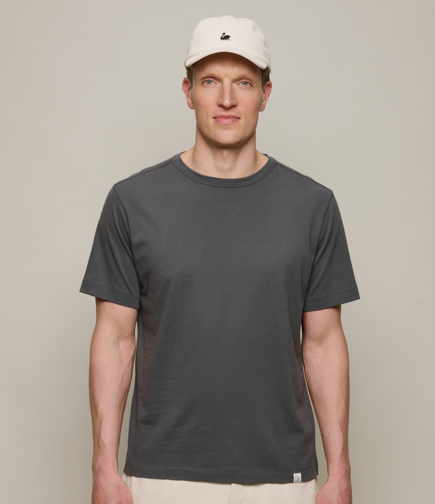 Man wearing a dark gray t-shirt and beige cap against a plain background