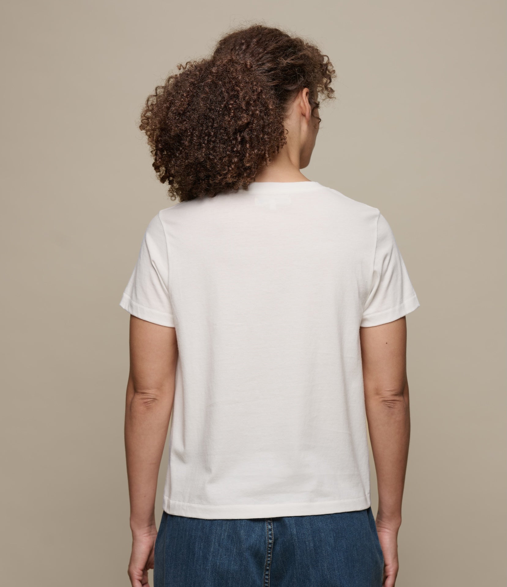 Person wearing a plain white t-shirt against a beige background