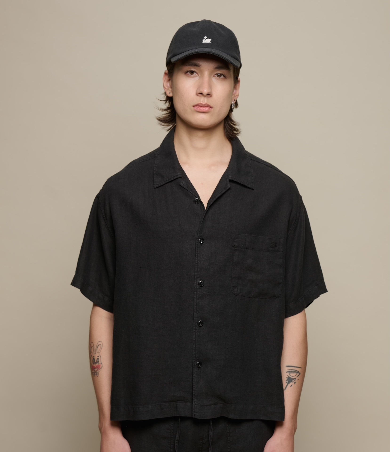 Person wearing a black short-sleeve linen shirt and cap against a beige background