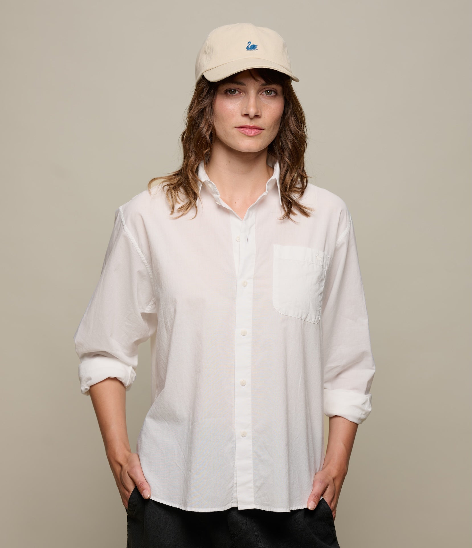 Woman wearing a white linen shirt and beige cap against a plain background
