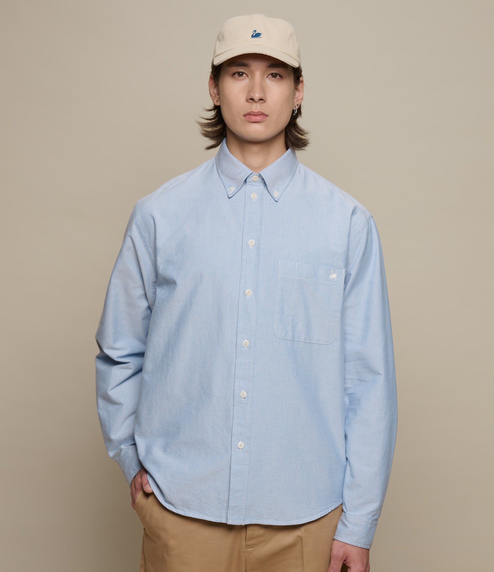 Person wearing a light blue button-down shirt and beige cap on a beige background